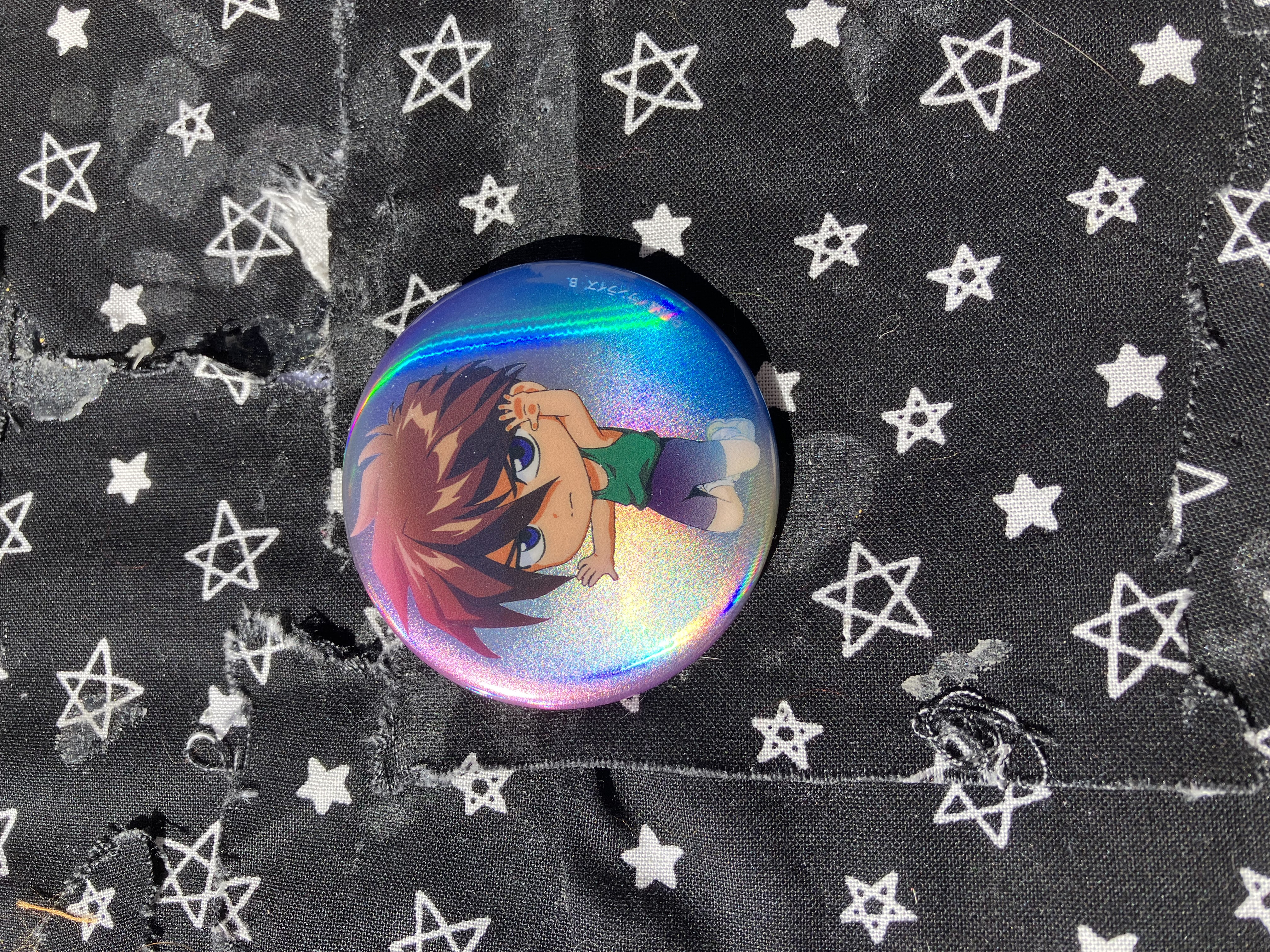 Holographic button that has chibi Gundam wing Heero in his green tanktop and black shorts.