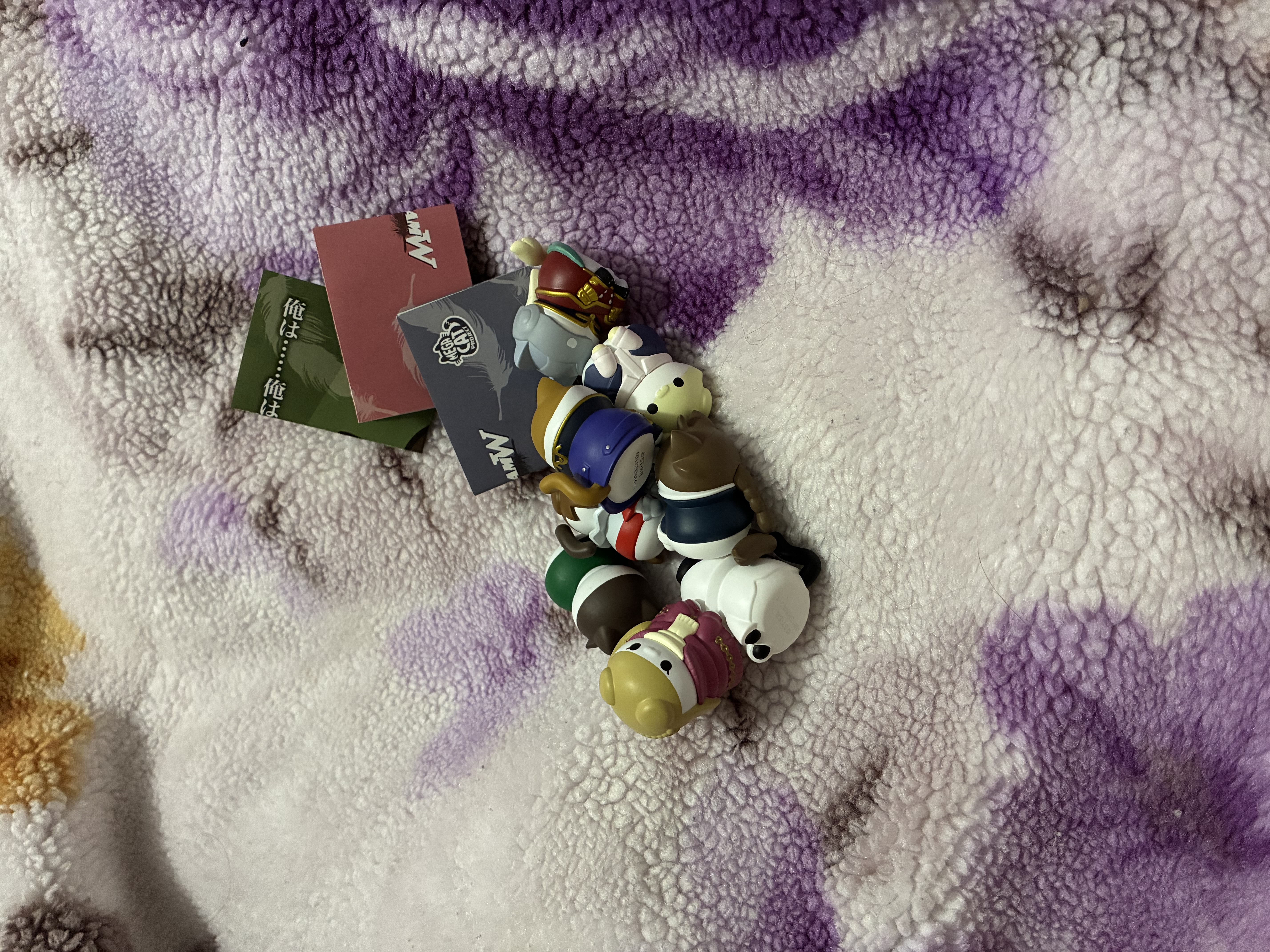 Pile of Gundam wing cat figures with three posters behind them.