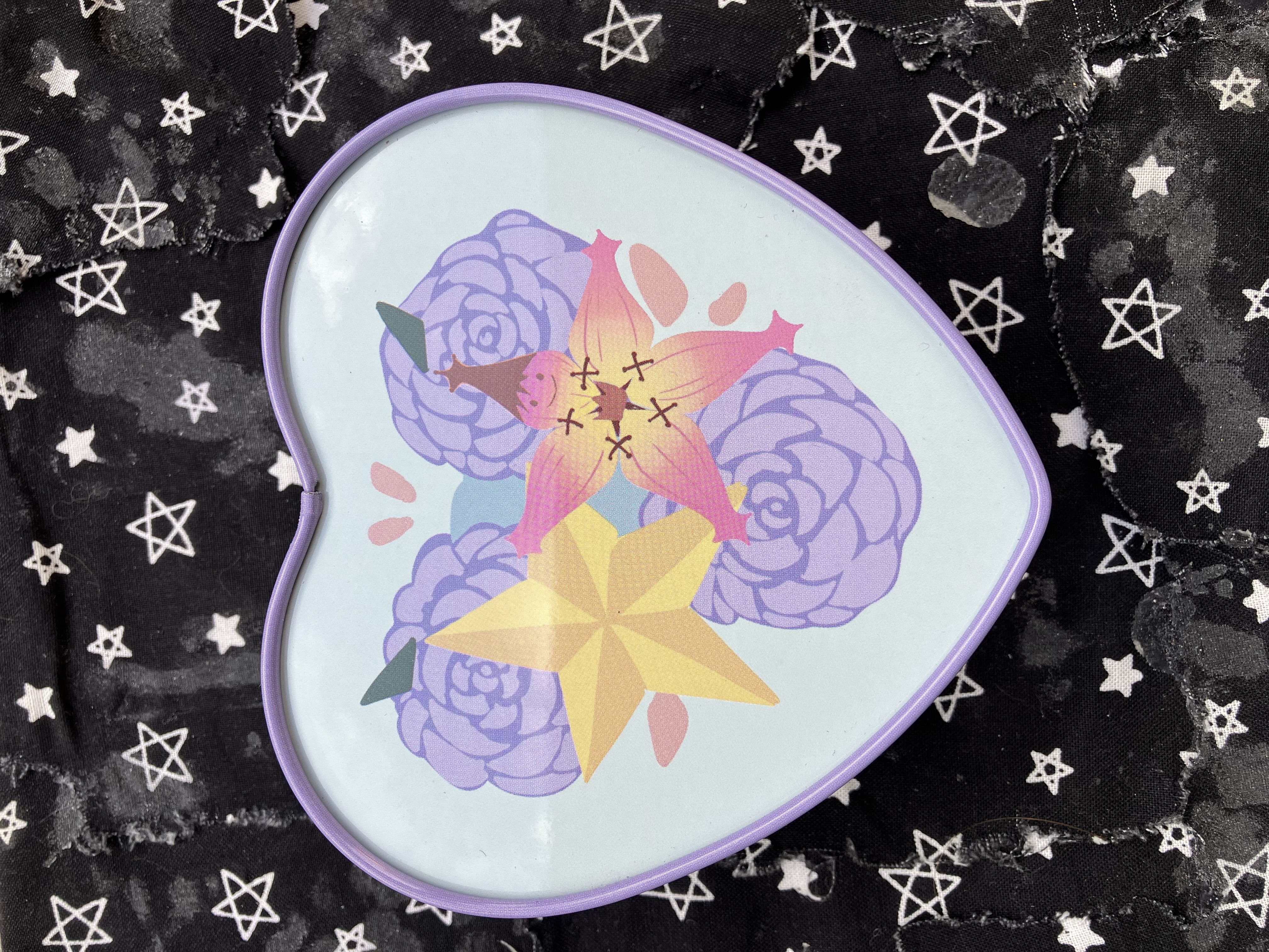 Bottom of trinket case with the Kingdom hearts lucky charms with purple flower behind them.