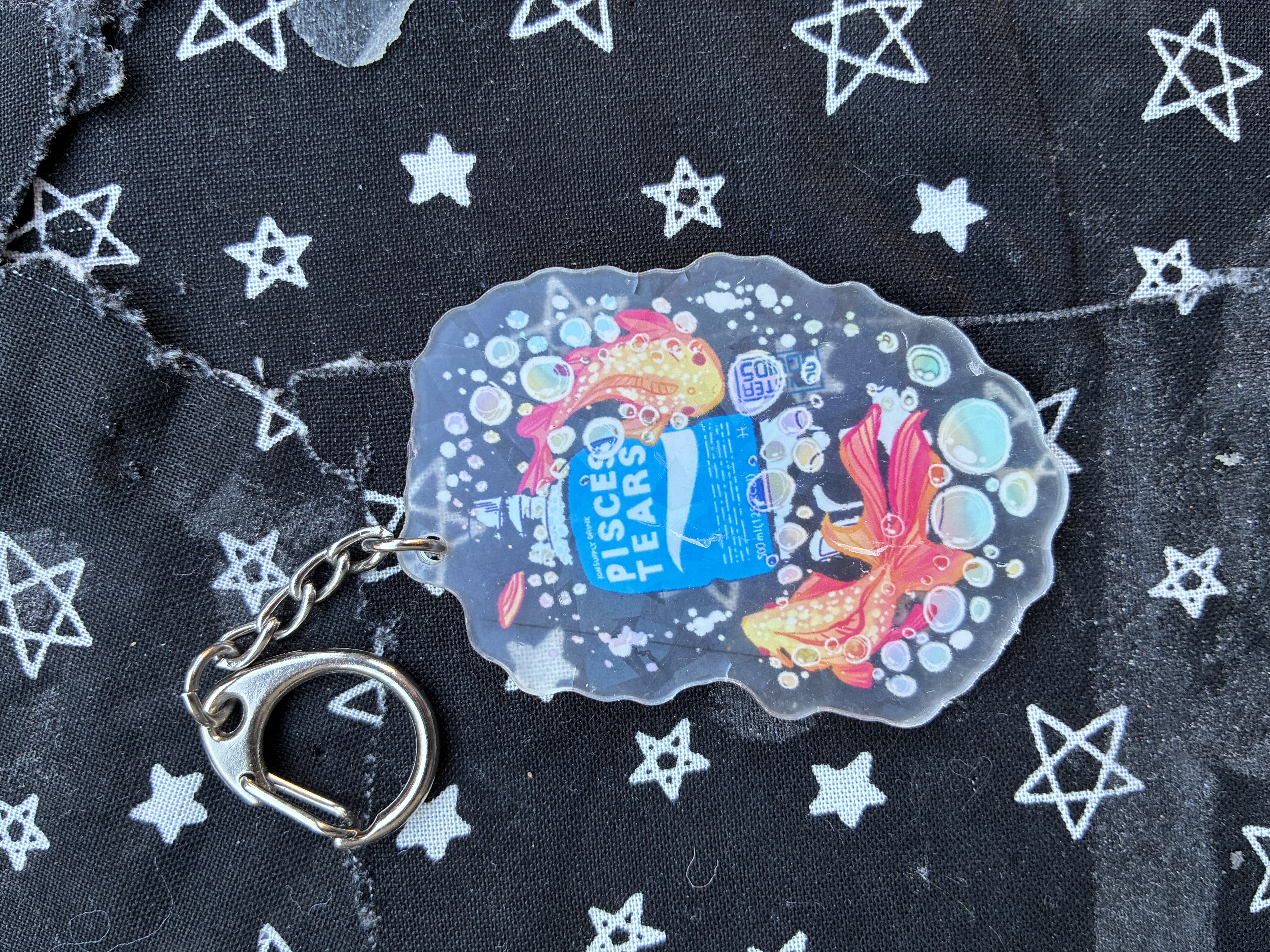 Acrylic charm of a bottle that reads pisces tears surrounded with bubbles and two fishes.