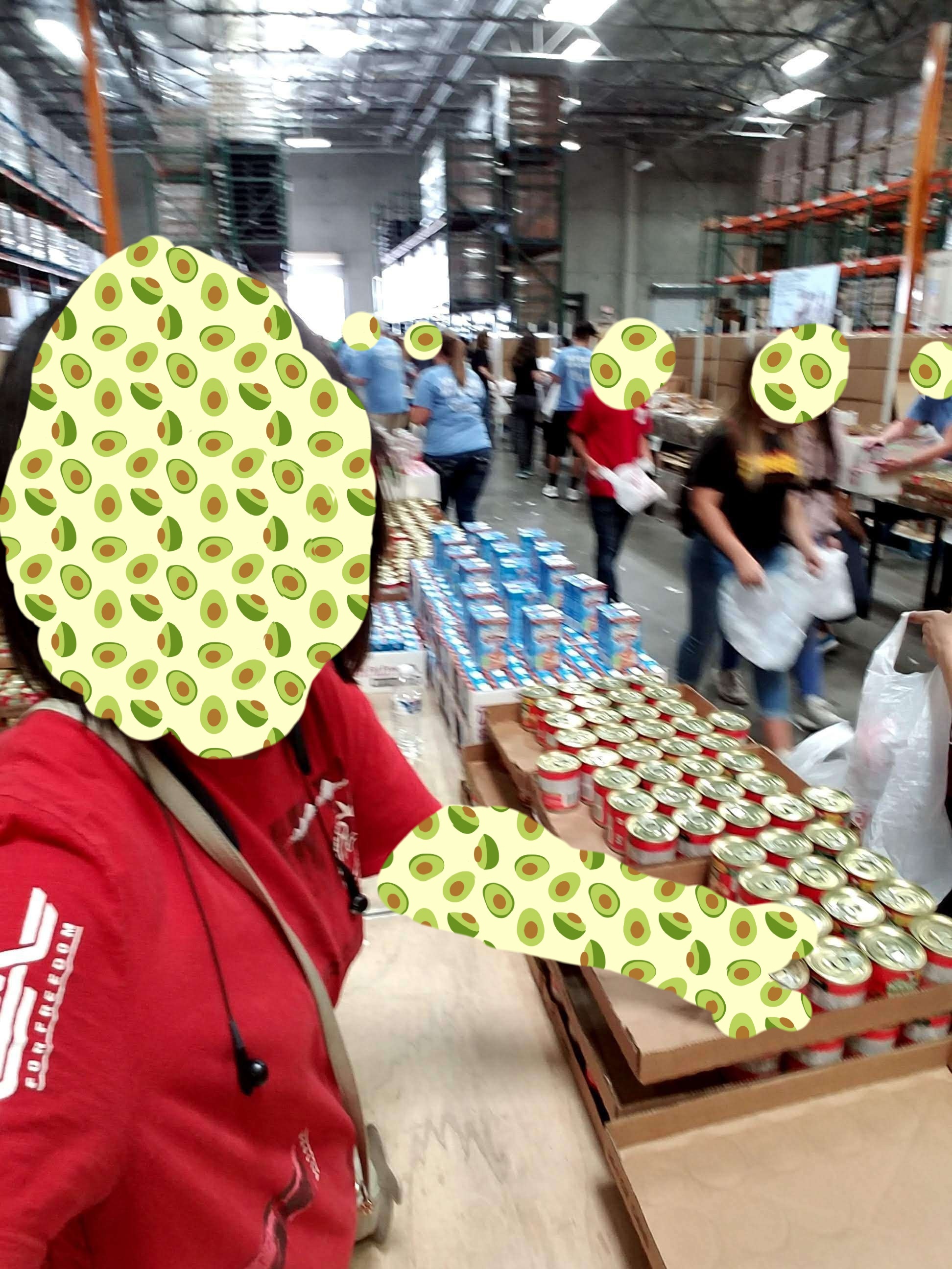Teen girl with black hair and avocado wallpaper on her face hands out canned ravioli in a crowd of fellow volunteers.