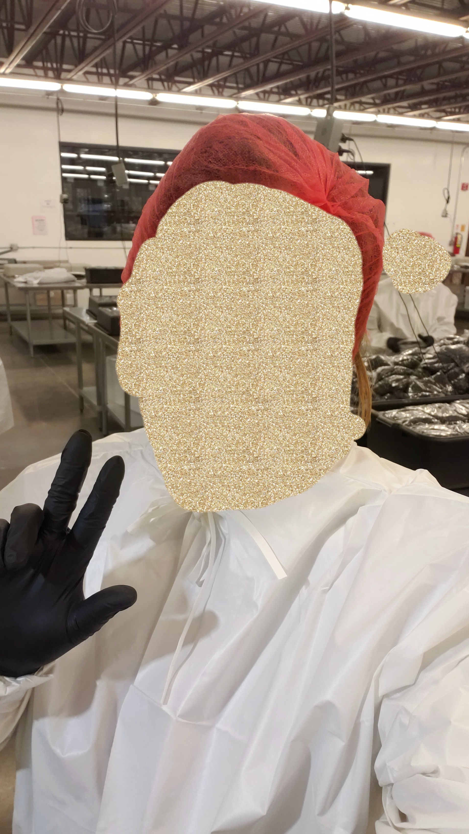 Girl wears red hairnet, white smock, glitter gold wallpaper on her face, and black gloves with a peace sign.