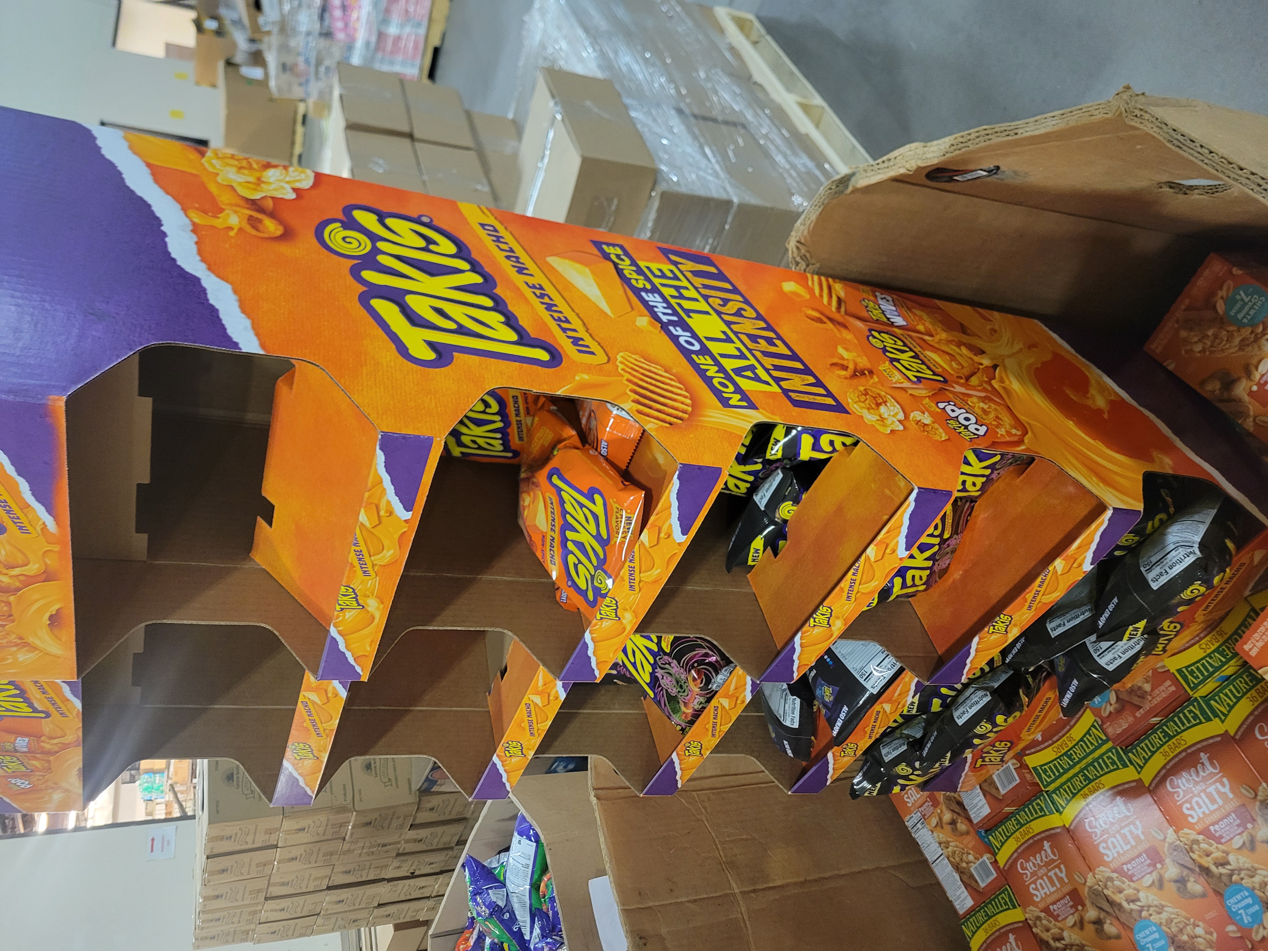 Mostly empty Takis chips display stacked on top of boxes of granola bars.
