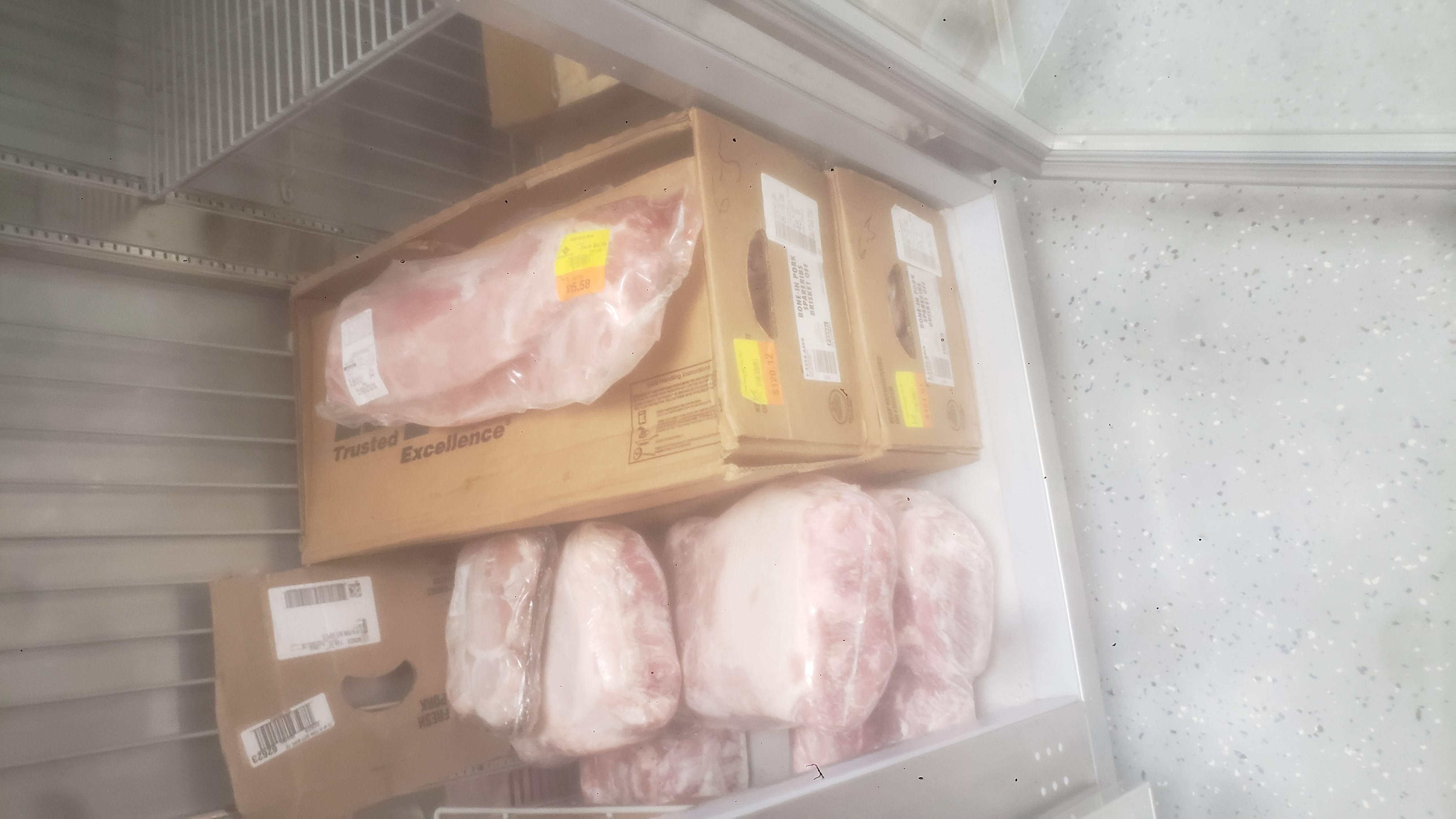 Packs of meat with some on the bottom and on top of cardboard boxes in a fridge.