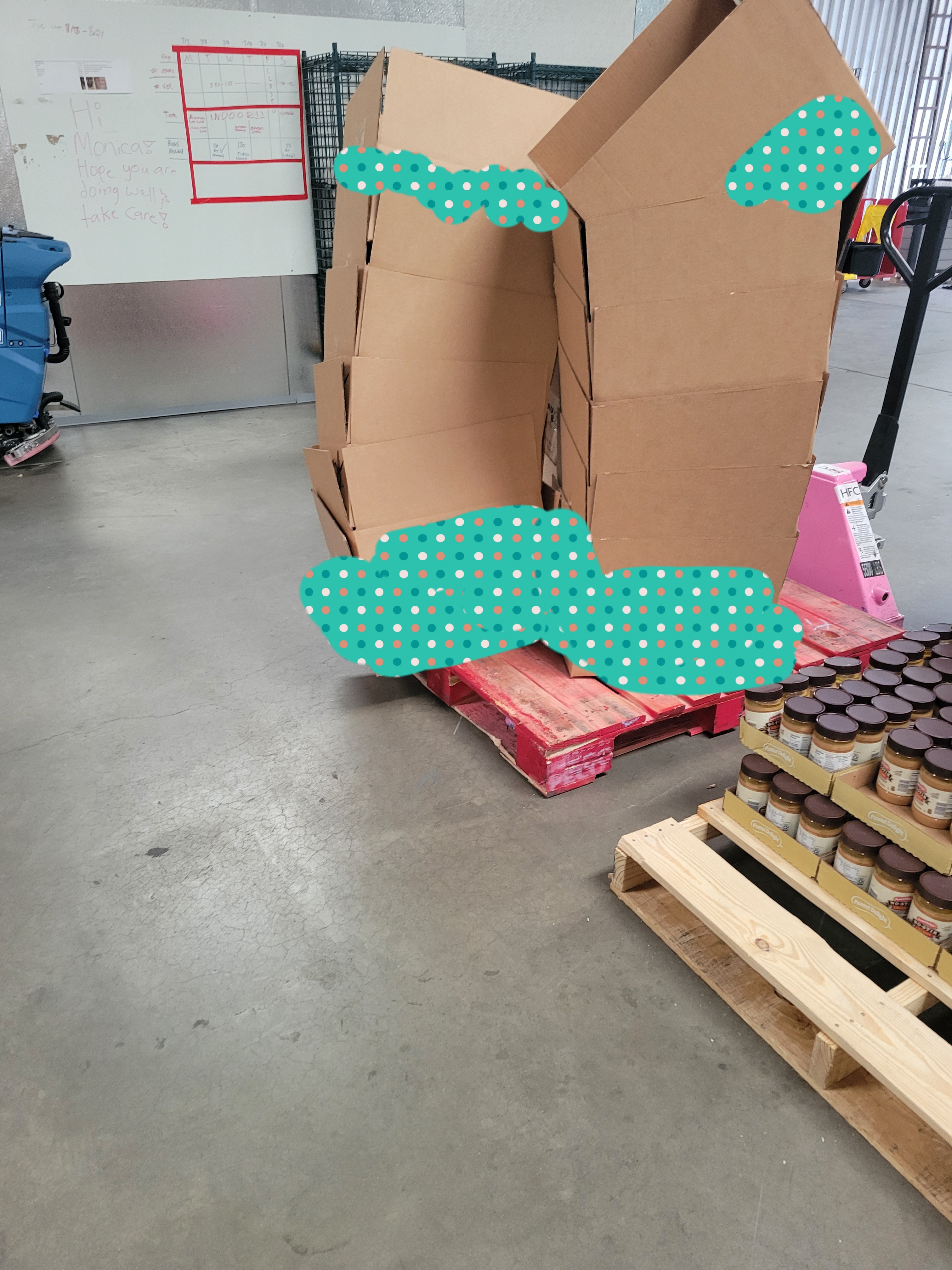 Cardboard boxes on one pallet and trays of jars of peanut butter on another next to it.