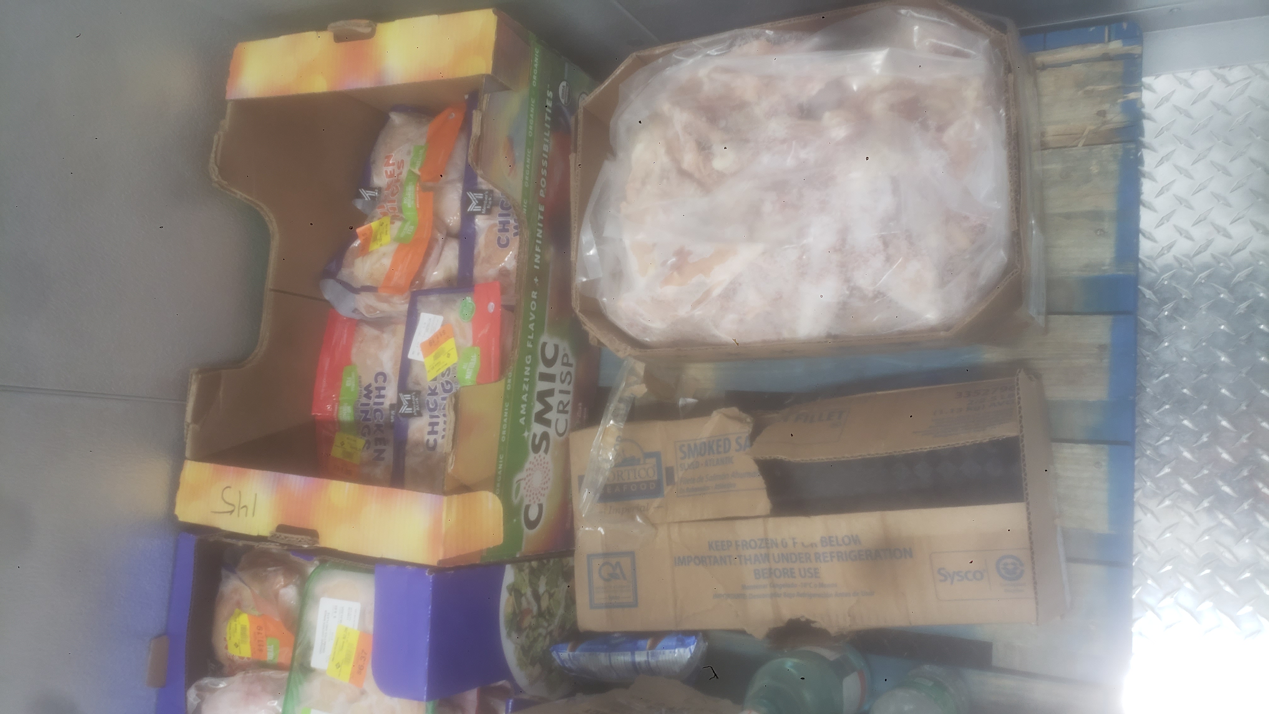 Bottle of water and sprite next to boxes and trays of various meats on a pallet.