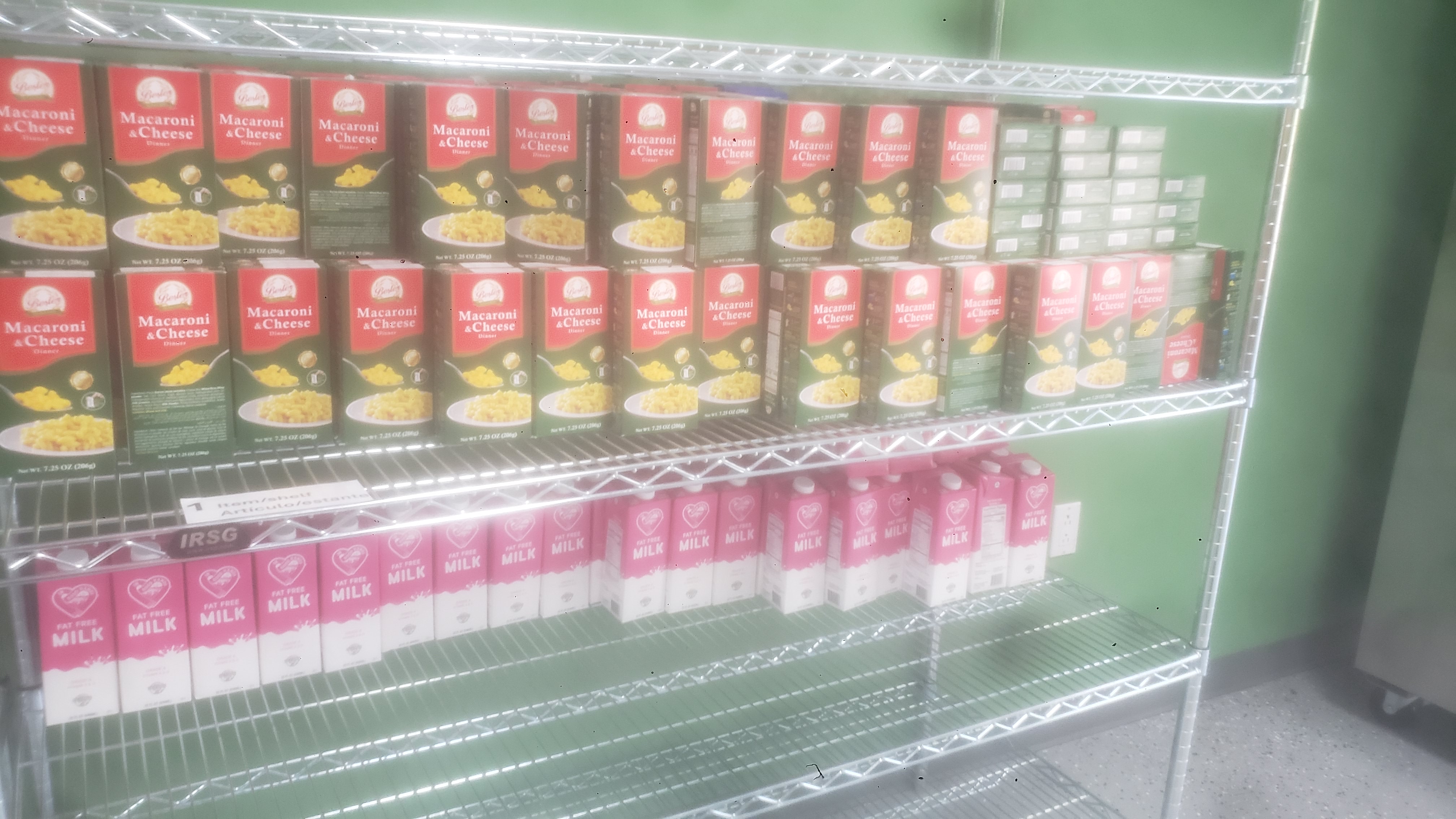 Boxes of mac n cheese and cartons of fat-free milk on a shelf.