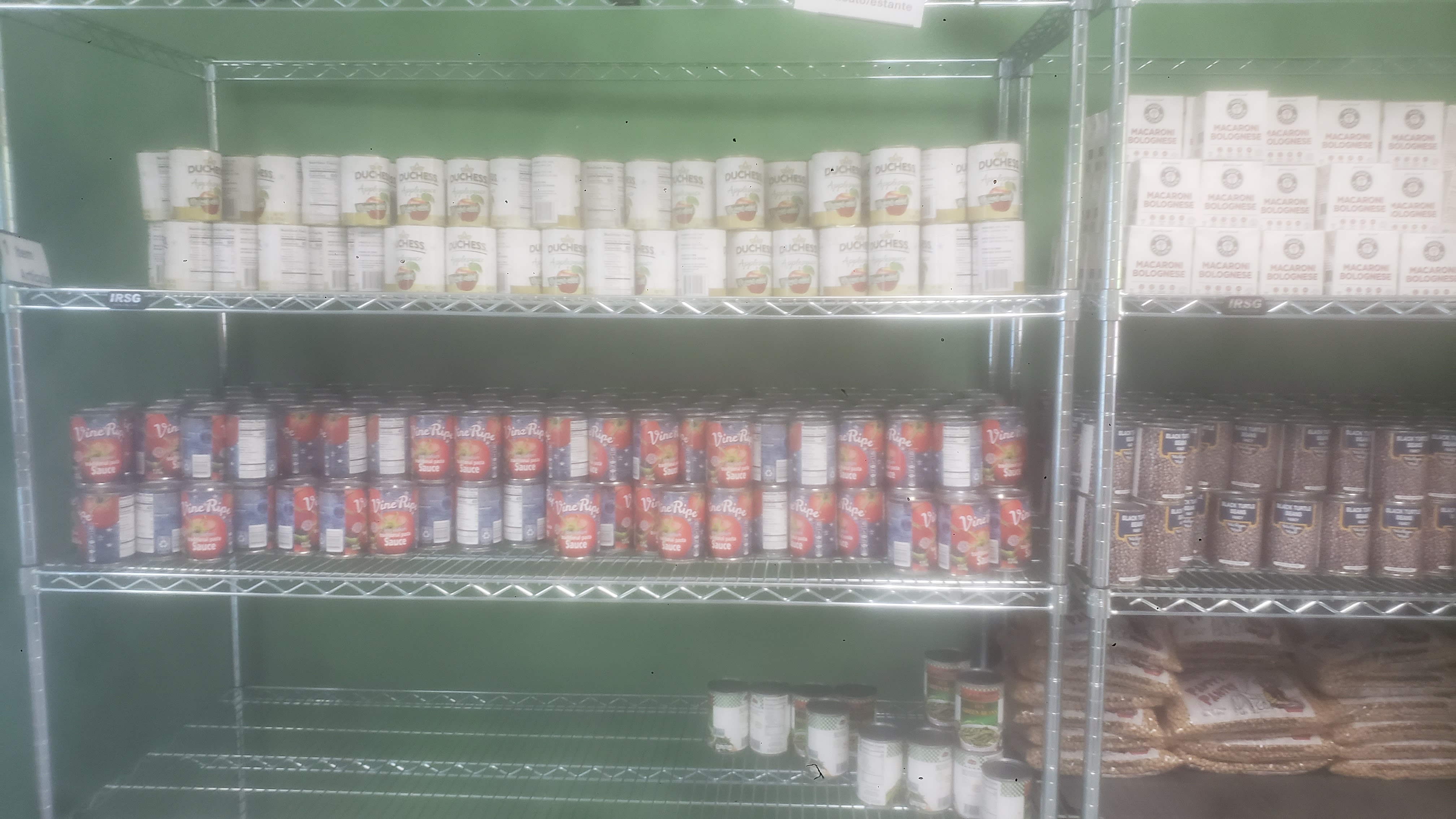 Canned applesauces, canned tomatoes sauces, and canned green beans on a four tier shelf.