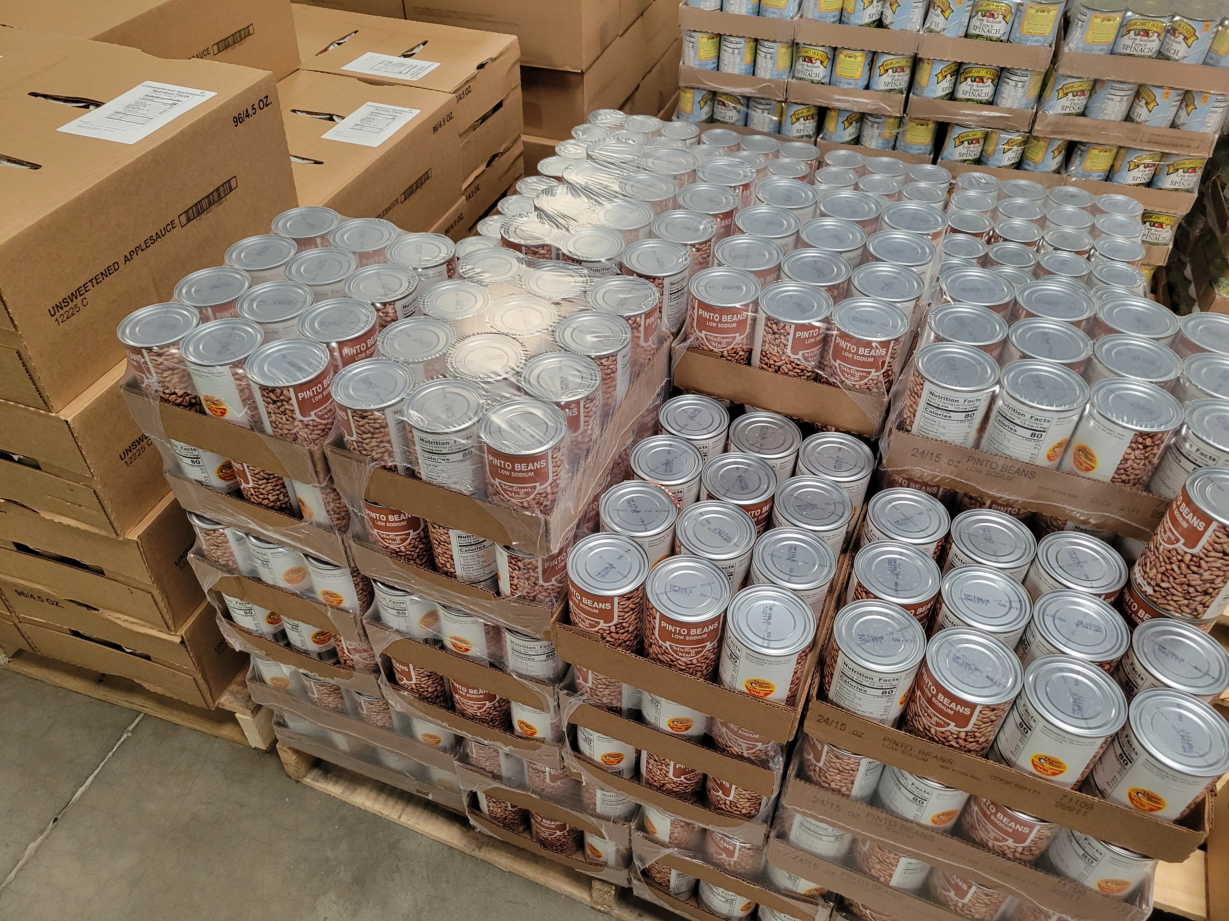 Pallet of canned pinto beans next to pallet of unsweeted applesauce and a pallet of canned spinach behind it.