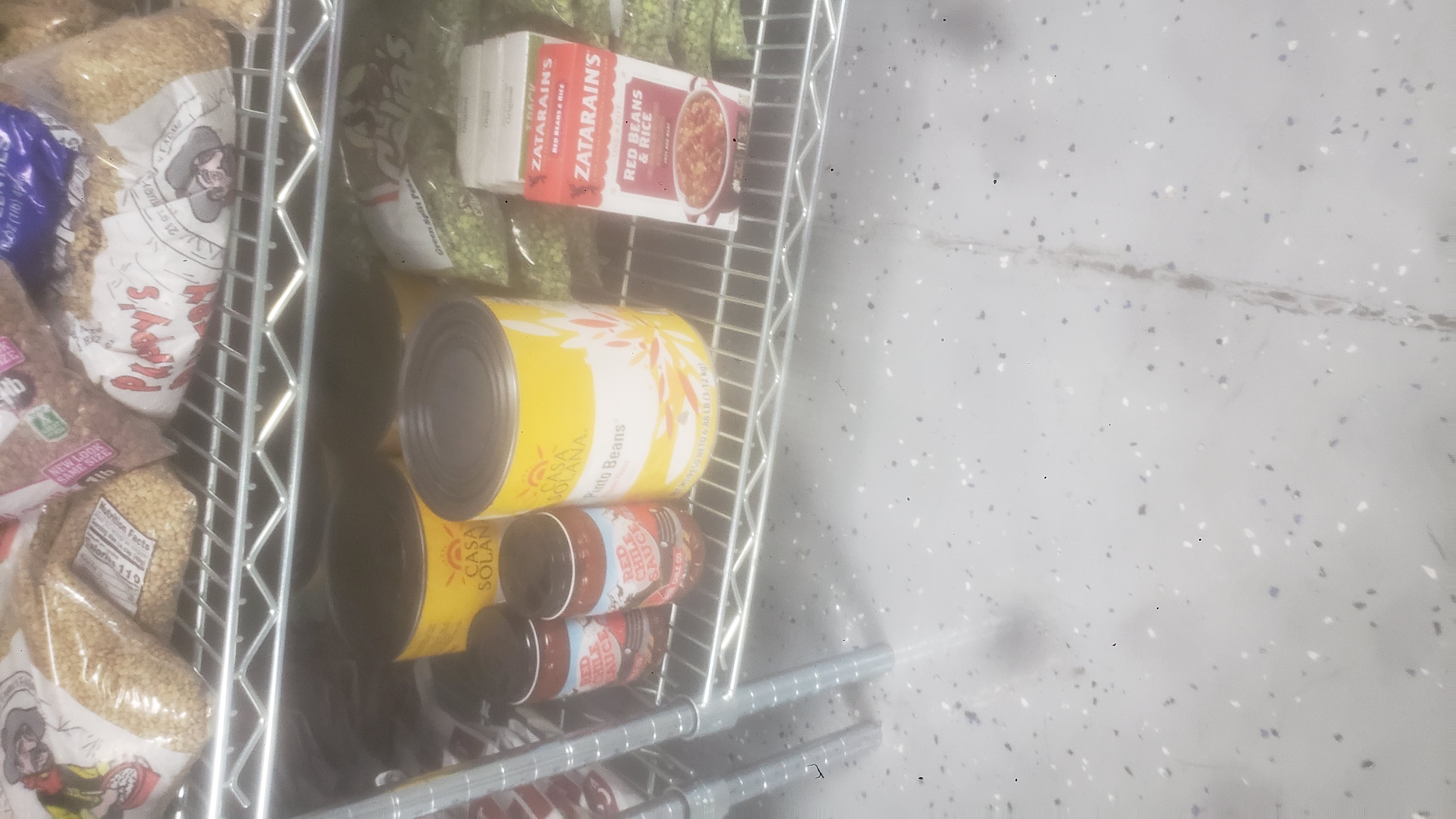 Jars of red chile sauce, #10 cans of pinto beans, box of red beans and rice, and bags of green split peas on a shelf.