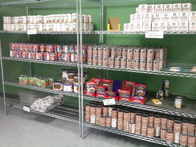 Two shelves filled with canned goods, boxes of red beans and rice, pouches of meat and a plastic tub filled with bags of dried cranberries.