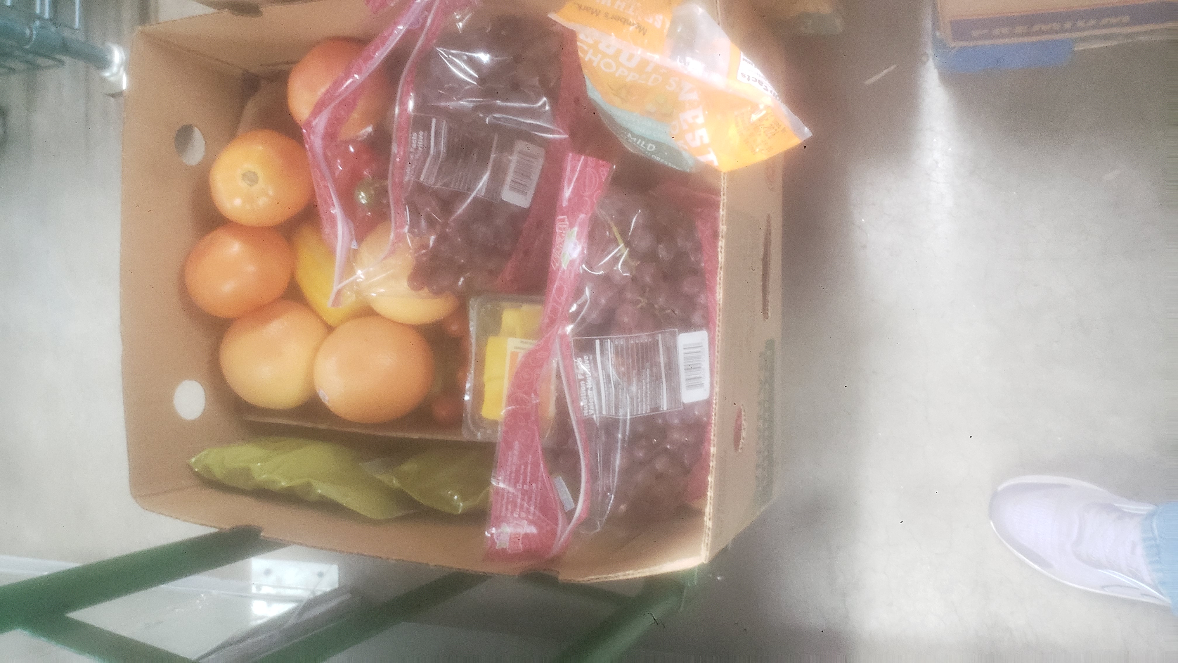 Banana box with no lid filled with grapes, tomatoes, and other mixed produce on a cart.
