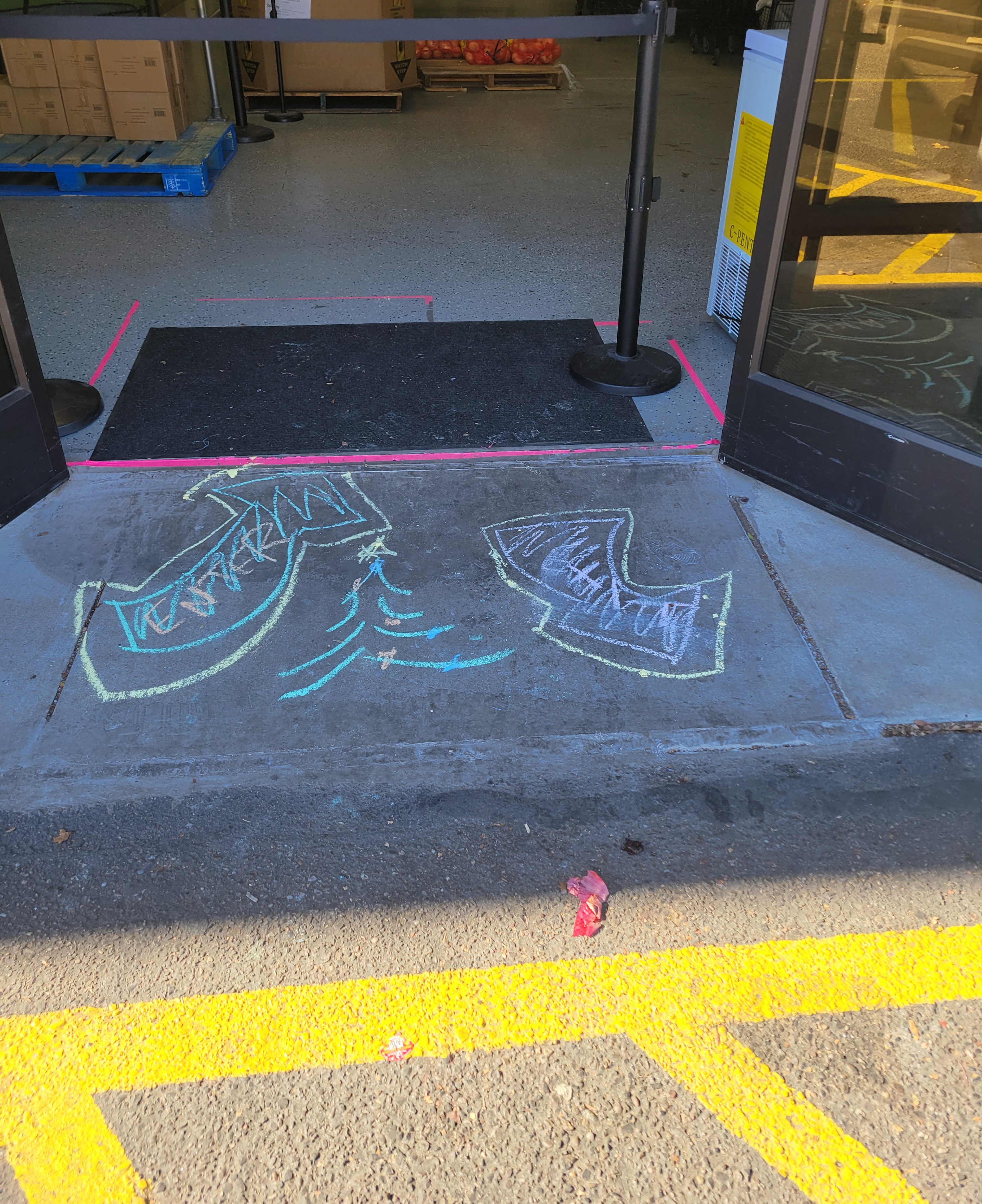 Side walk with chalk drawing of arrows pointing in and out. There is a retractable belt stanchion on top of it.