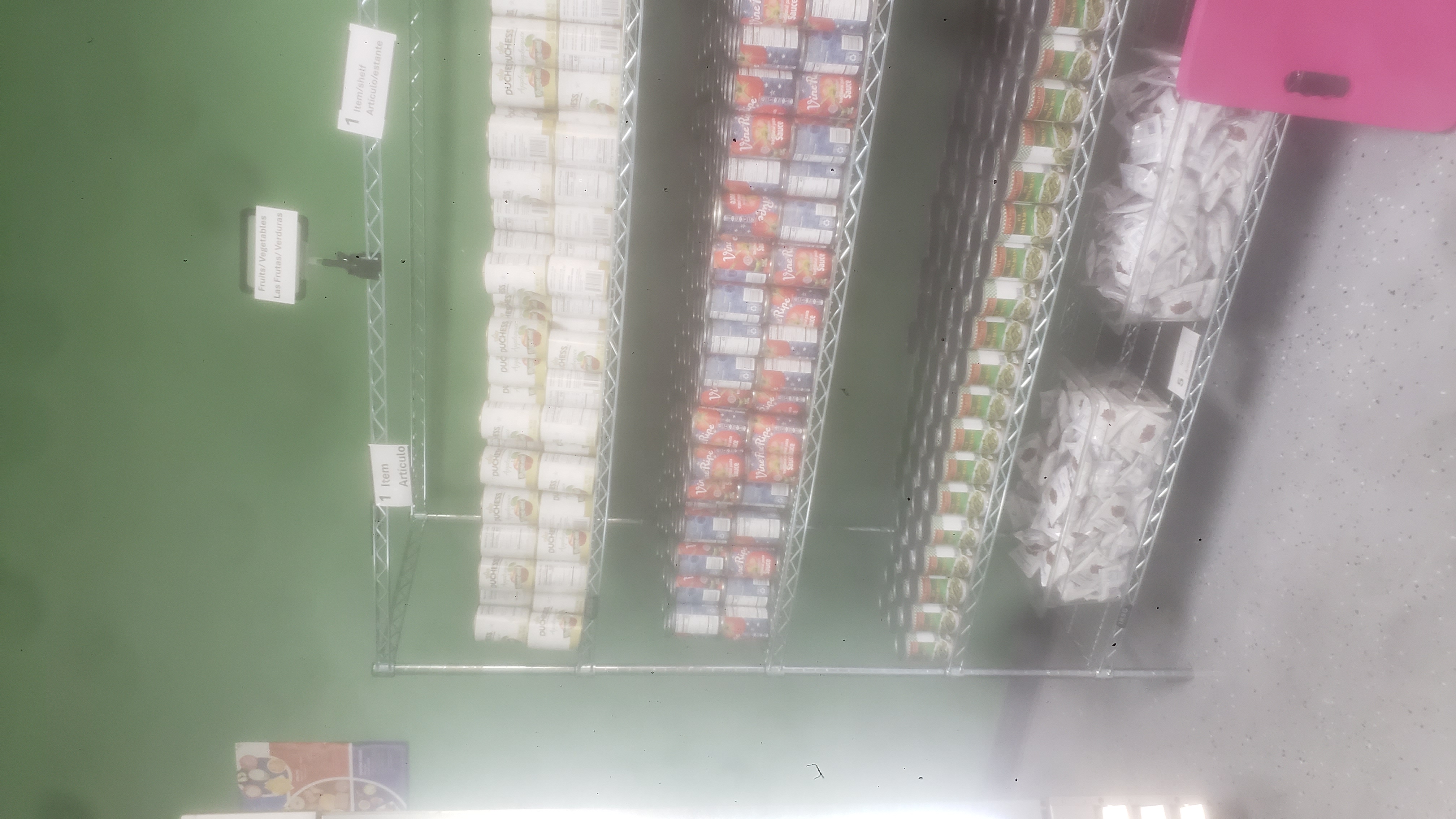 Canned applesauces, canned tomatoes sauces, packets of dried cranberries, and canned green beans on a four tier shelf.