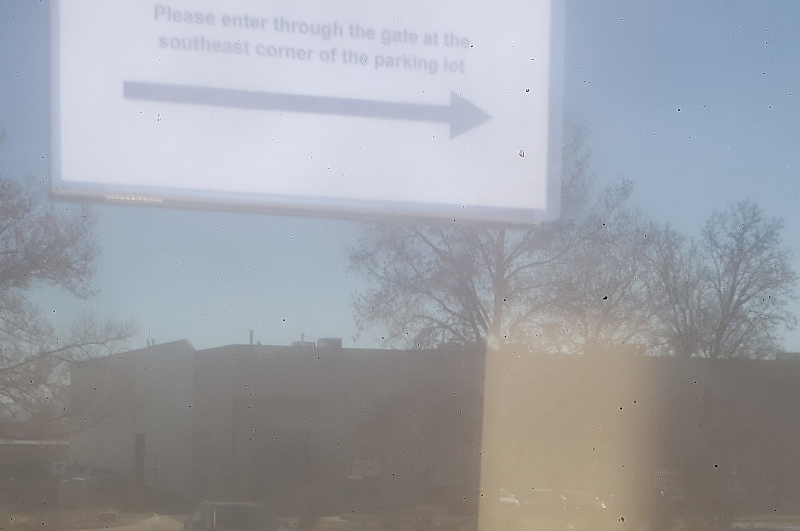 A sign that says please enter through the gate at the southeast corner of the parking lot with a arrow under it.