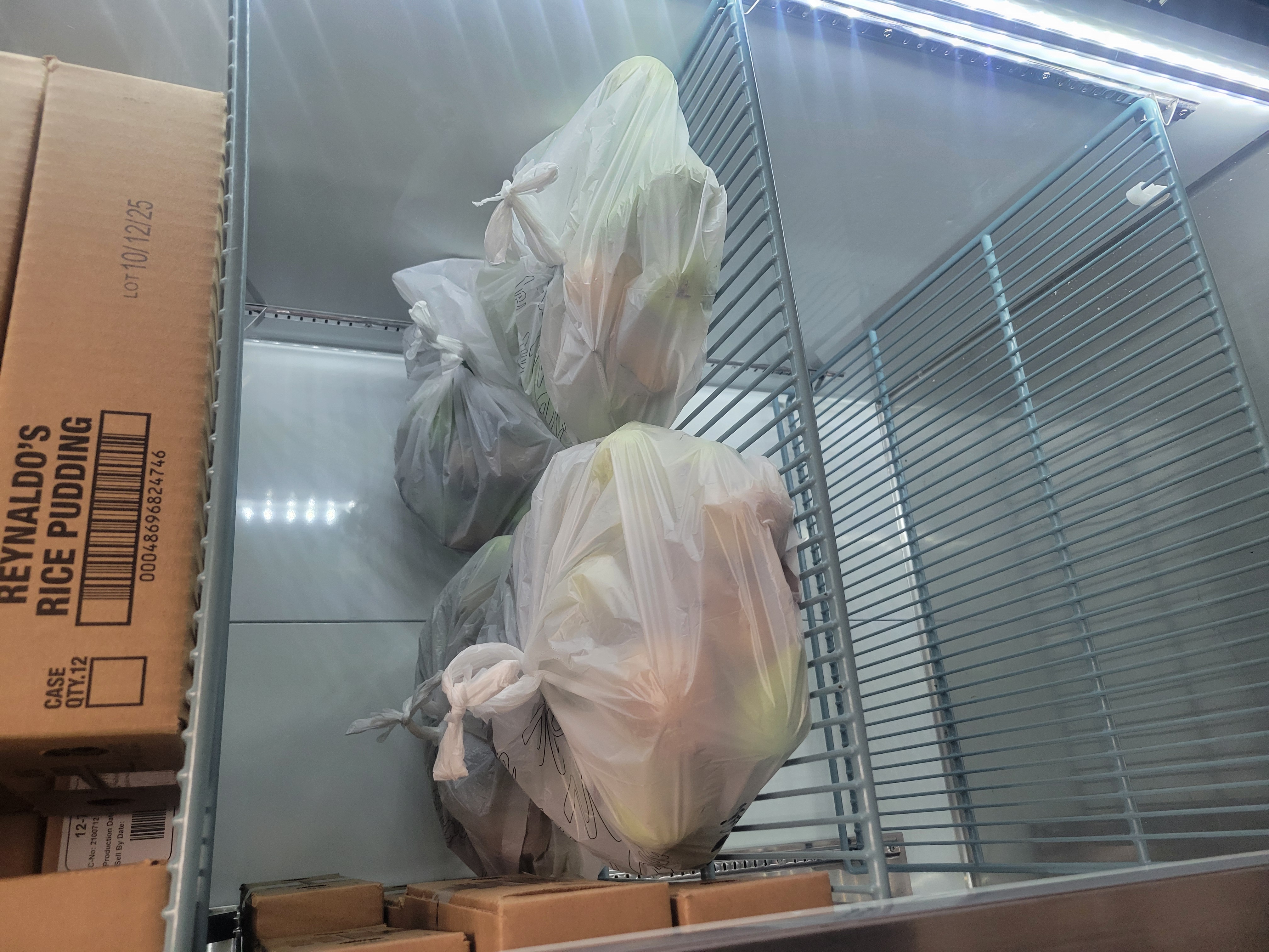 Boxes of rice pudding on the top shelf and bags of produce on the second shelf of a fridge.