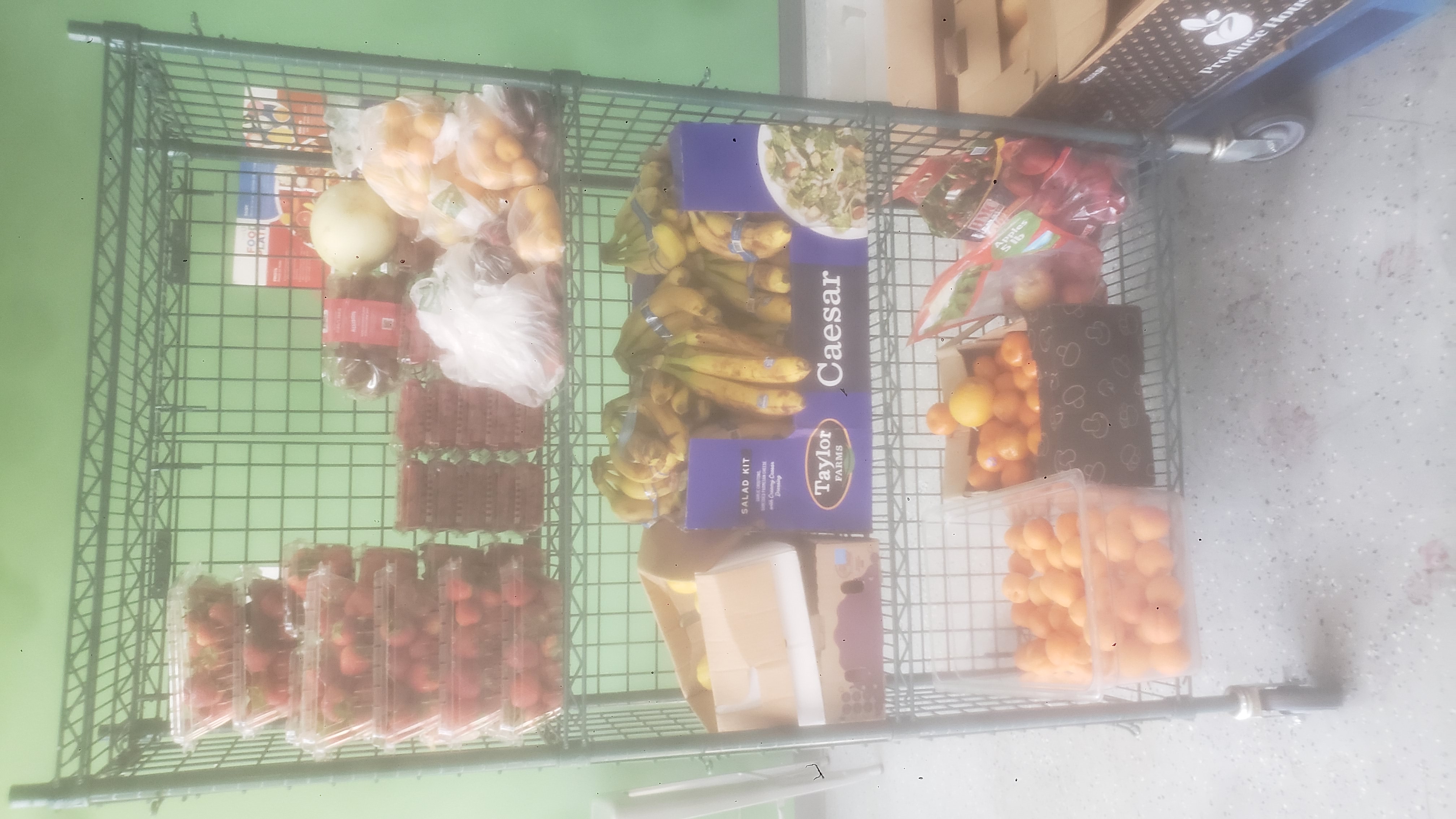 Various produce in bags, containers, trays, and plastic bin on three tier cage shelf.