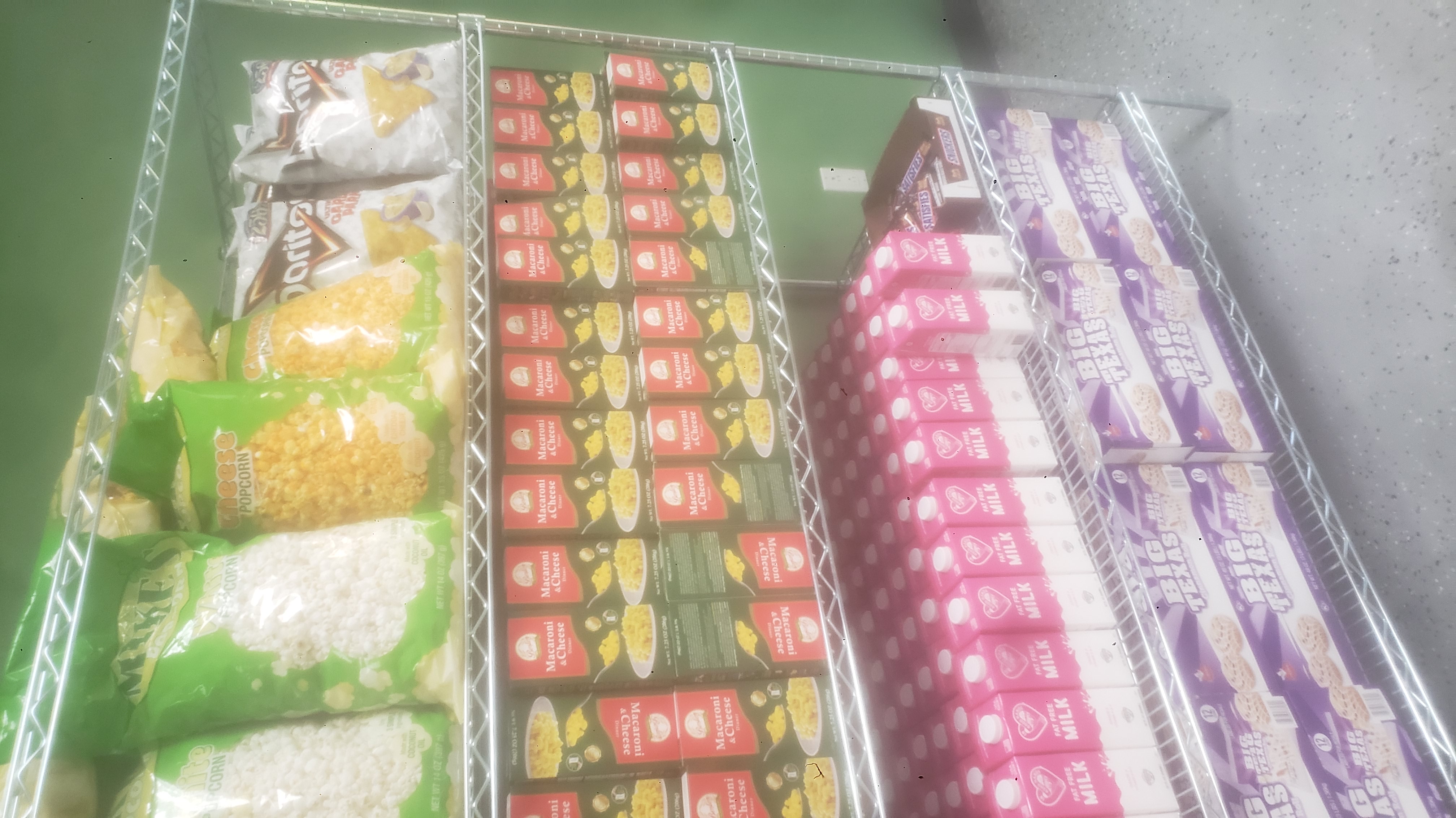 Boxes of mac n cheese, boxes of cinnamon rolls, cartons of fat-free milk on a shelf, bags of garlic parmesan chips, cheese popcorn, and white popcorn on a shelf.