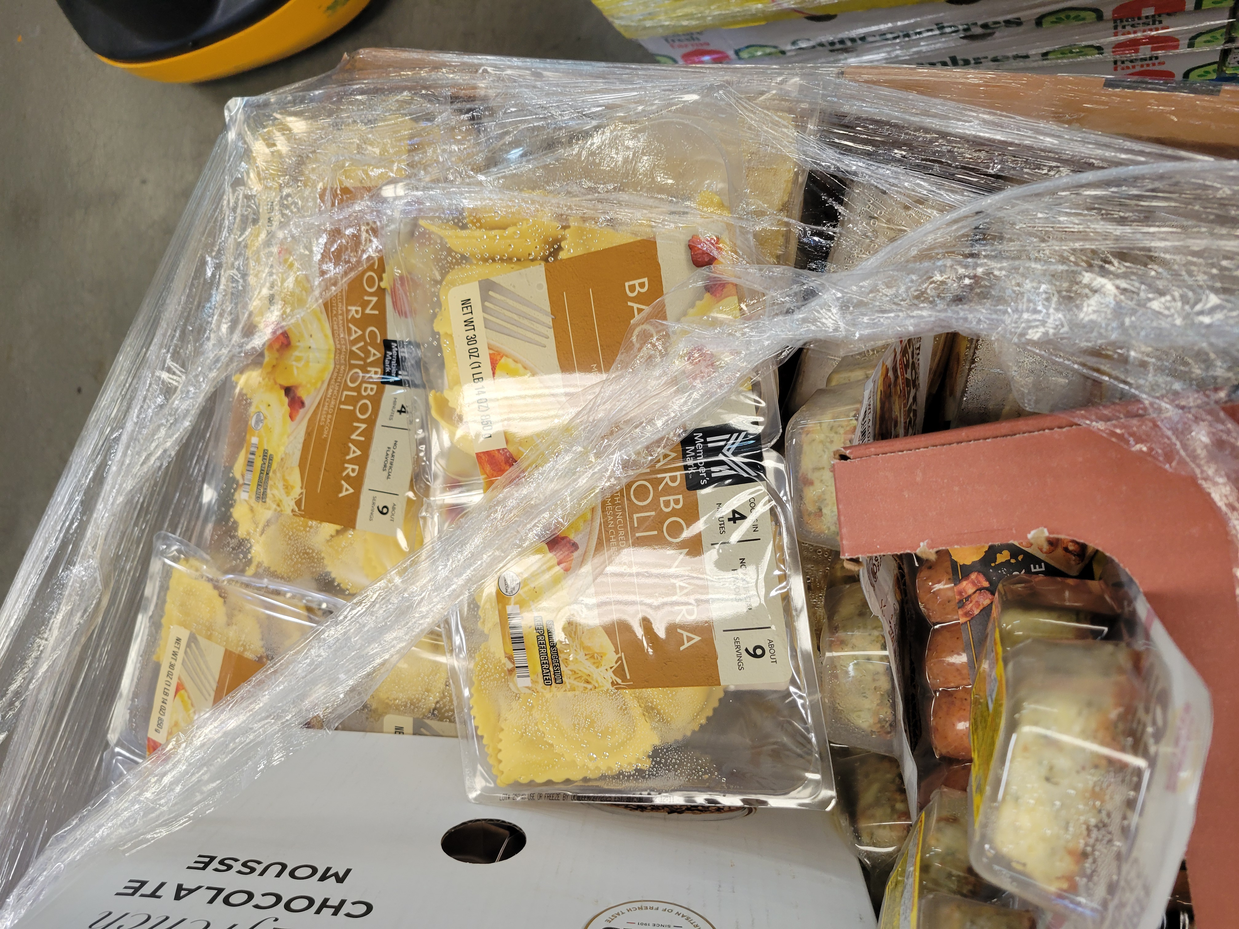 Packages of bacon carbonara ravoli on a food filled pallet next to box of chocolate mousse.