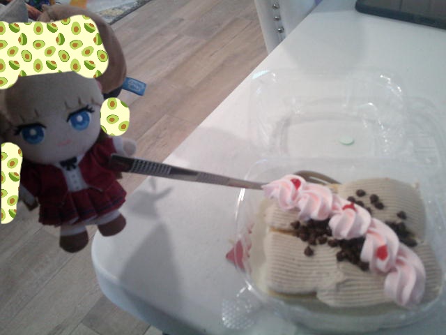 Hand holds Relena plush to look like she is holding a fork in a tres leches cake.