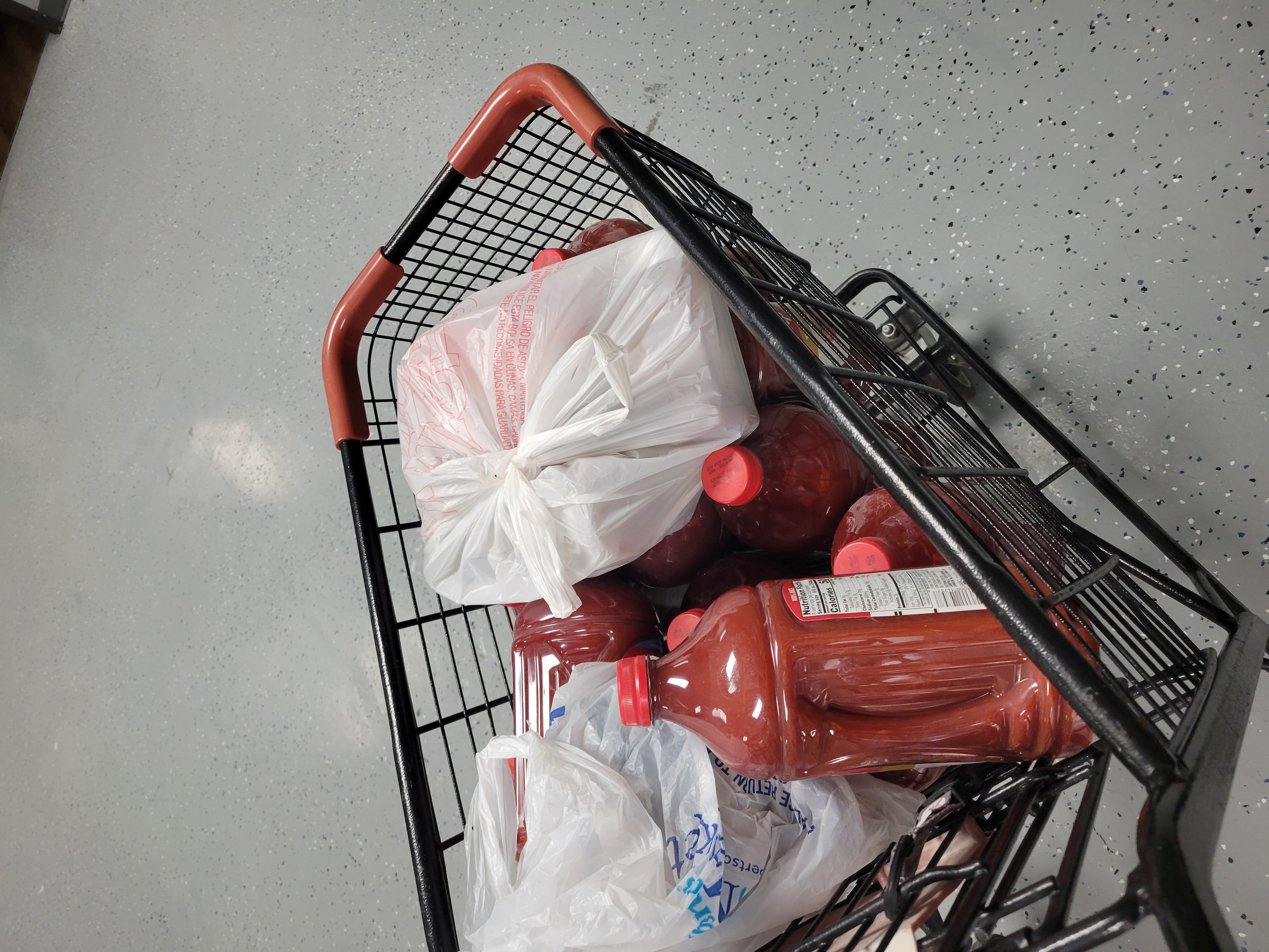 Shopping cart filled with gallons of tomato juice.