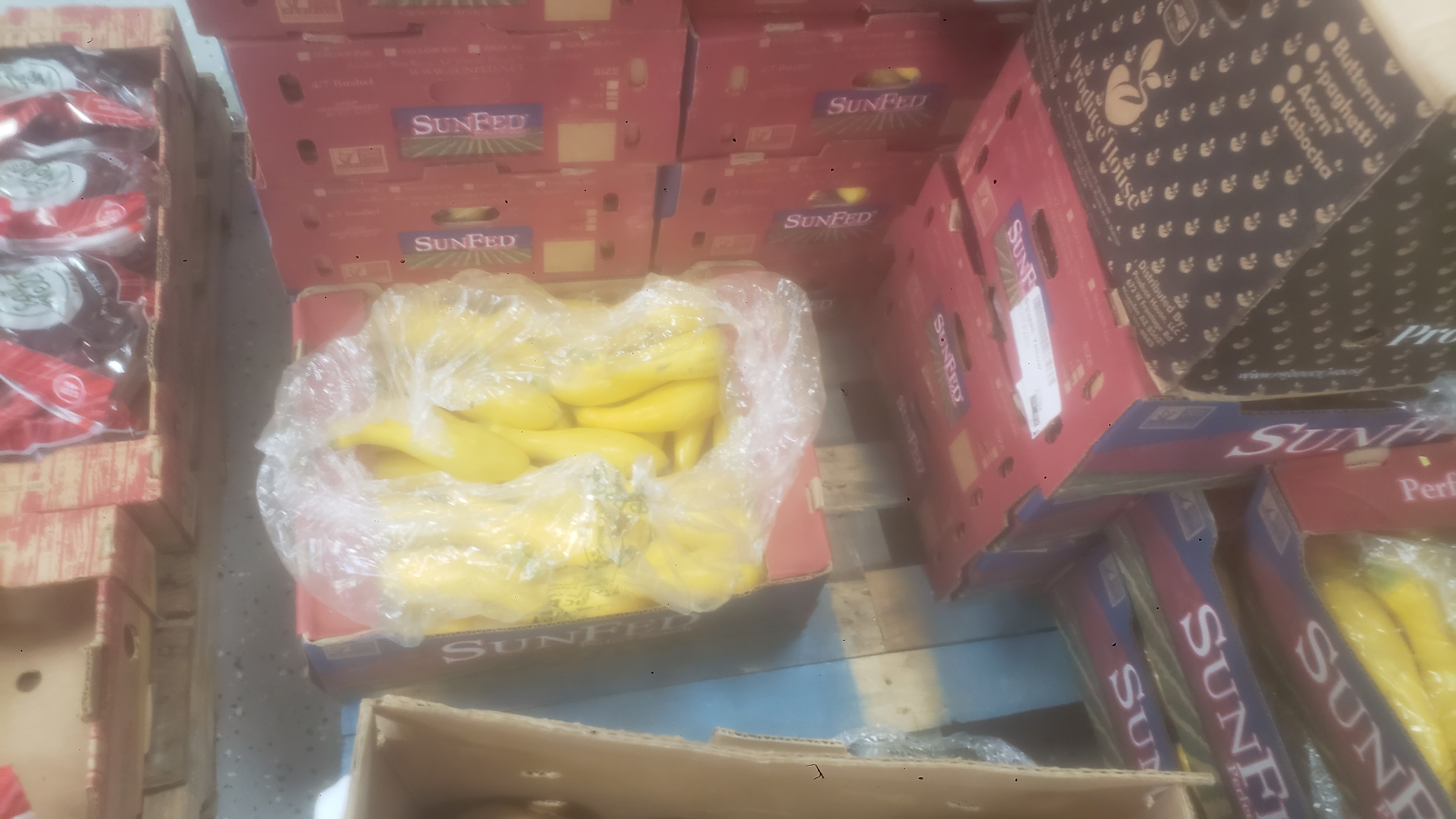 Cardboard boxes stacked on each other with one showing summer squashes covered in plastic.