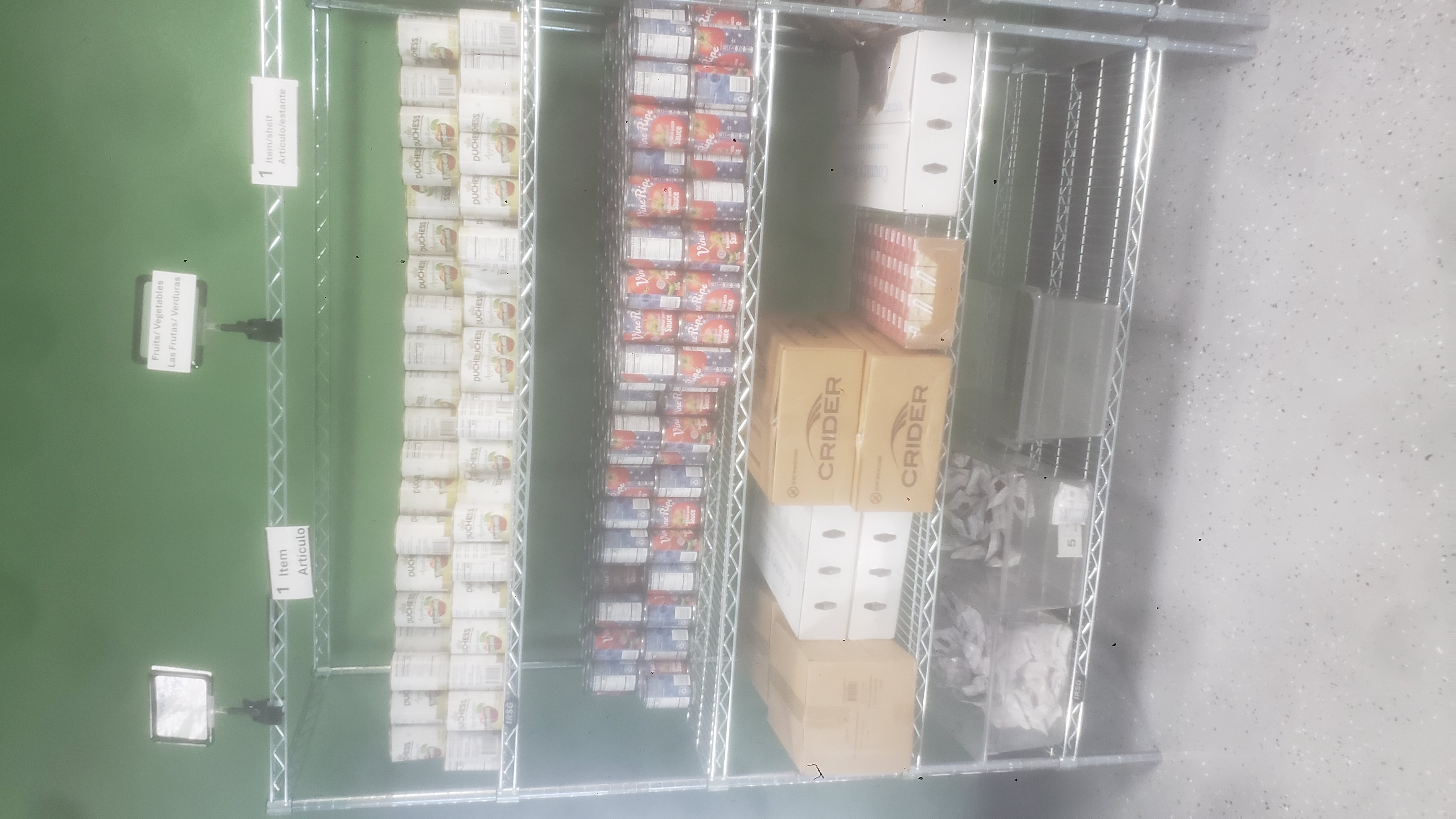 Cans of applesauce, cans of tomato sauce, packets of dried cranberries, box of applesauce, boxes of yogurt, boxes of chicken, and tray of juice boxes on racks of a shelf.