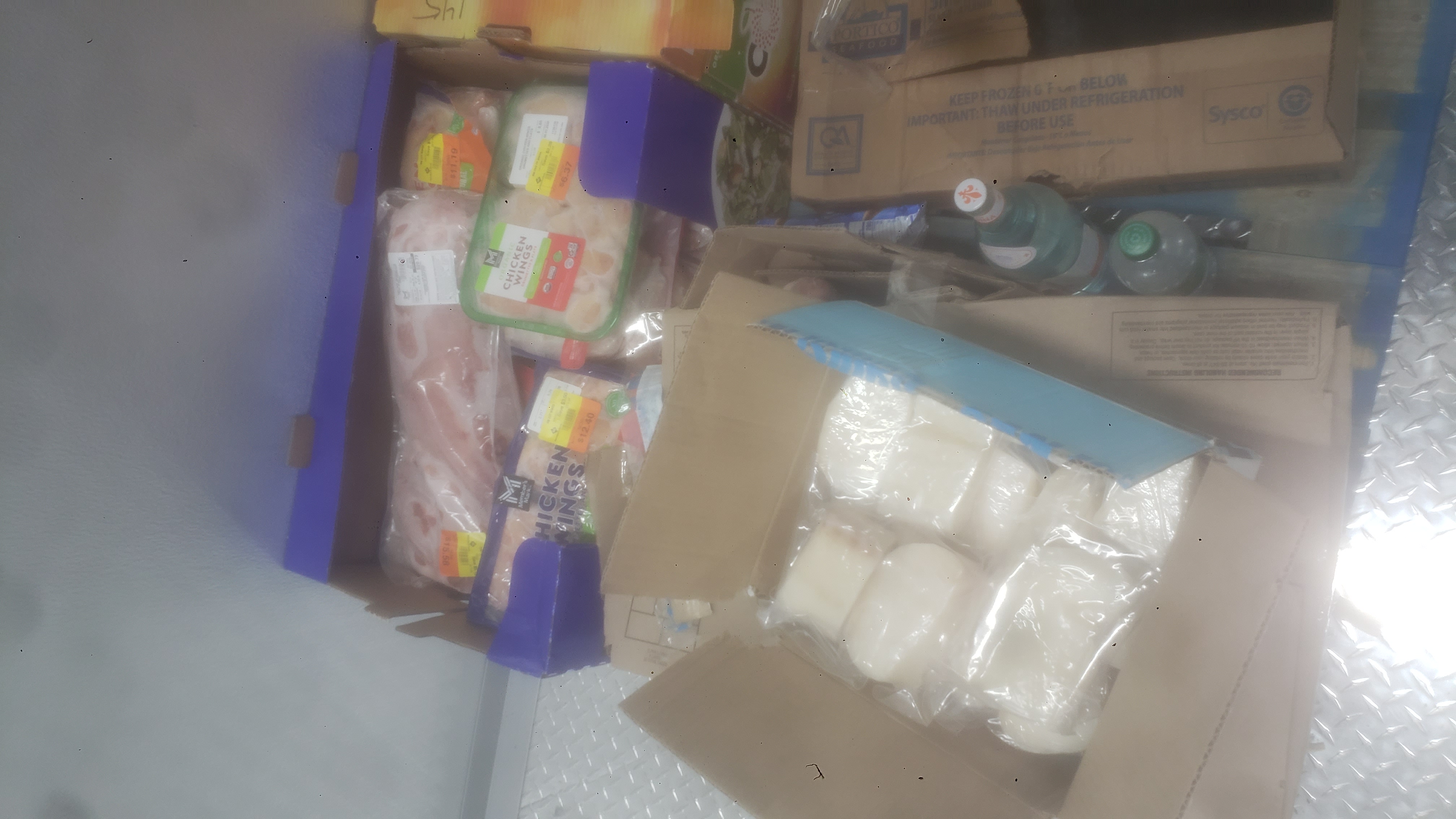 Bottle of water and sprite next to boxes and trays of various meats on a pallet.