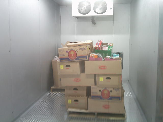Pallet of chicken and banana boxes full of food with another pallet that has a food filled cardboard container in a freezer box unit.