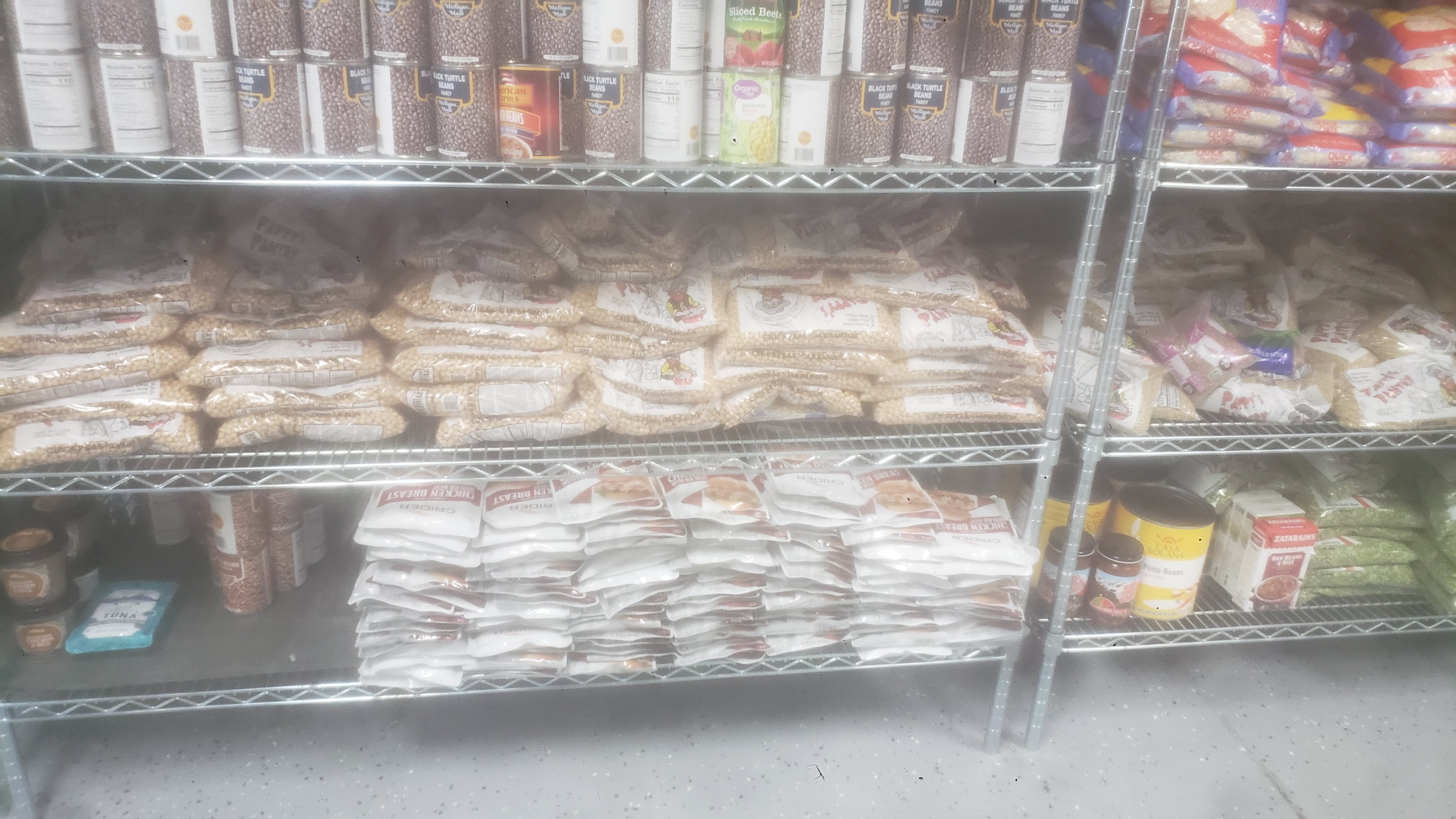 Cans of black turtle beans, bags of lentils, pouches of chicken breast, cans of pinto beans, and miscellaneous items on a shelf.