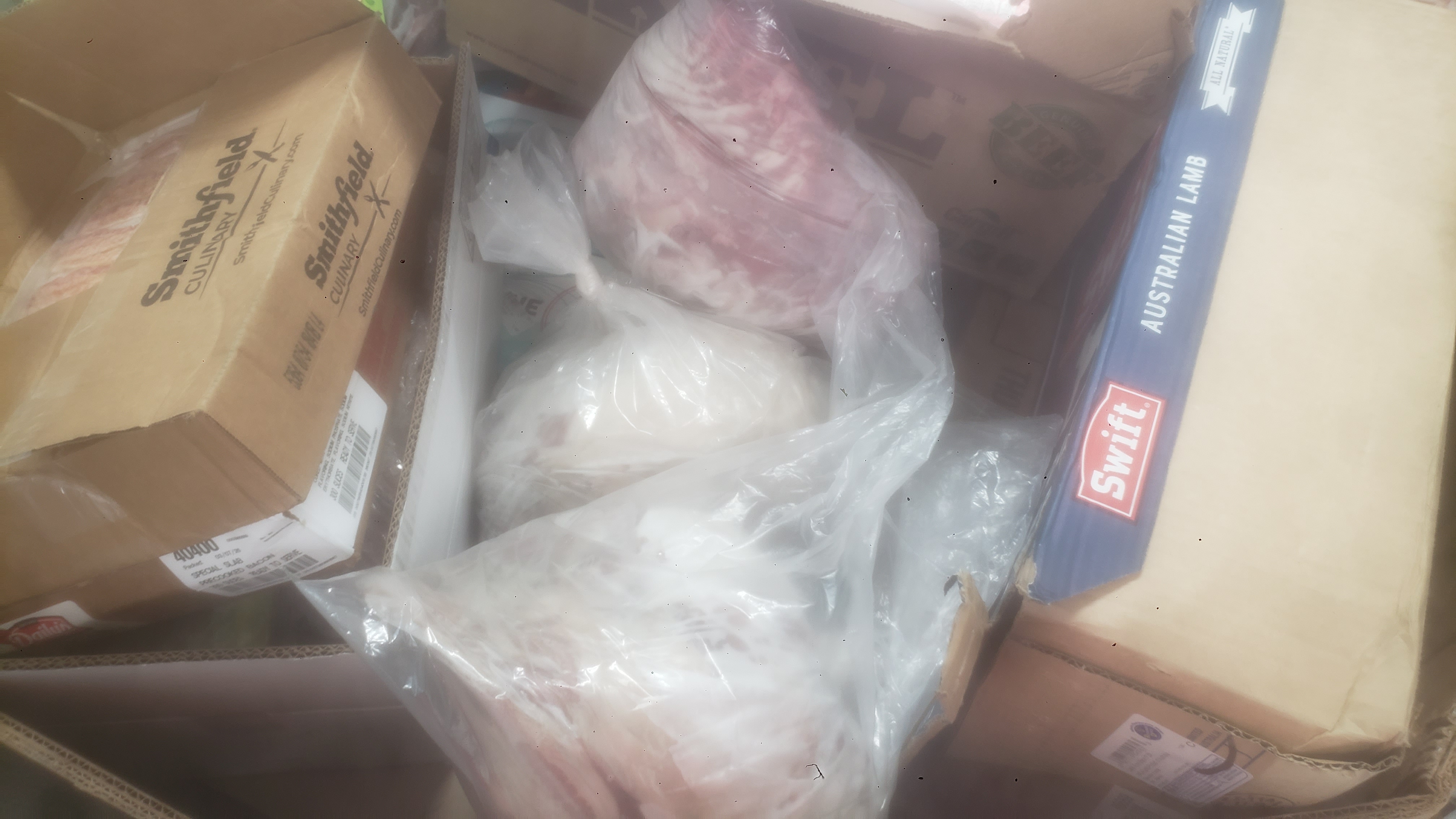Assorted frozen items in cardboard boxes such as lamb and bacon.