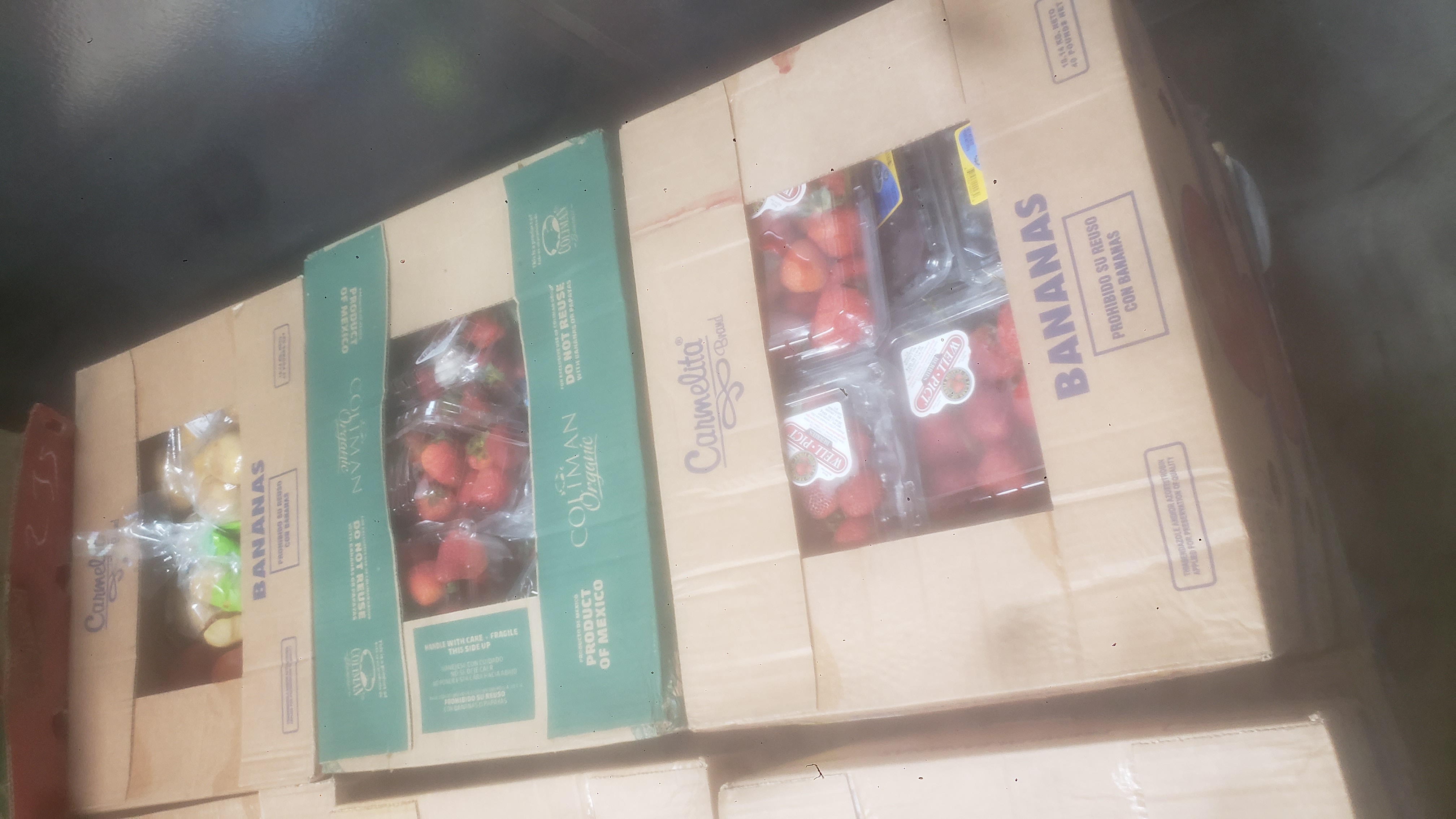 Banana boxes filled with various produce such as strawberries, blueberries, and potatoes.
