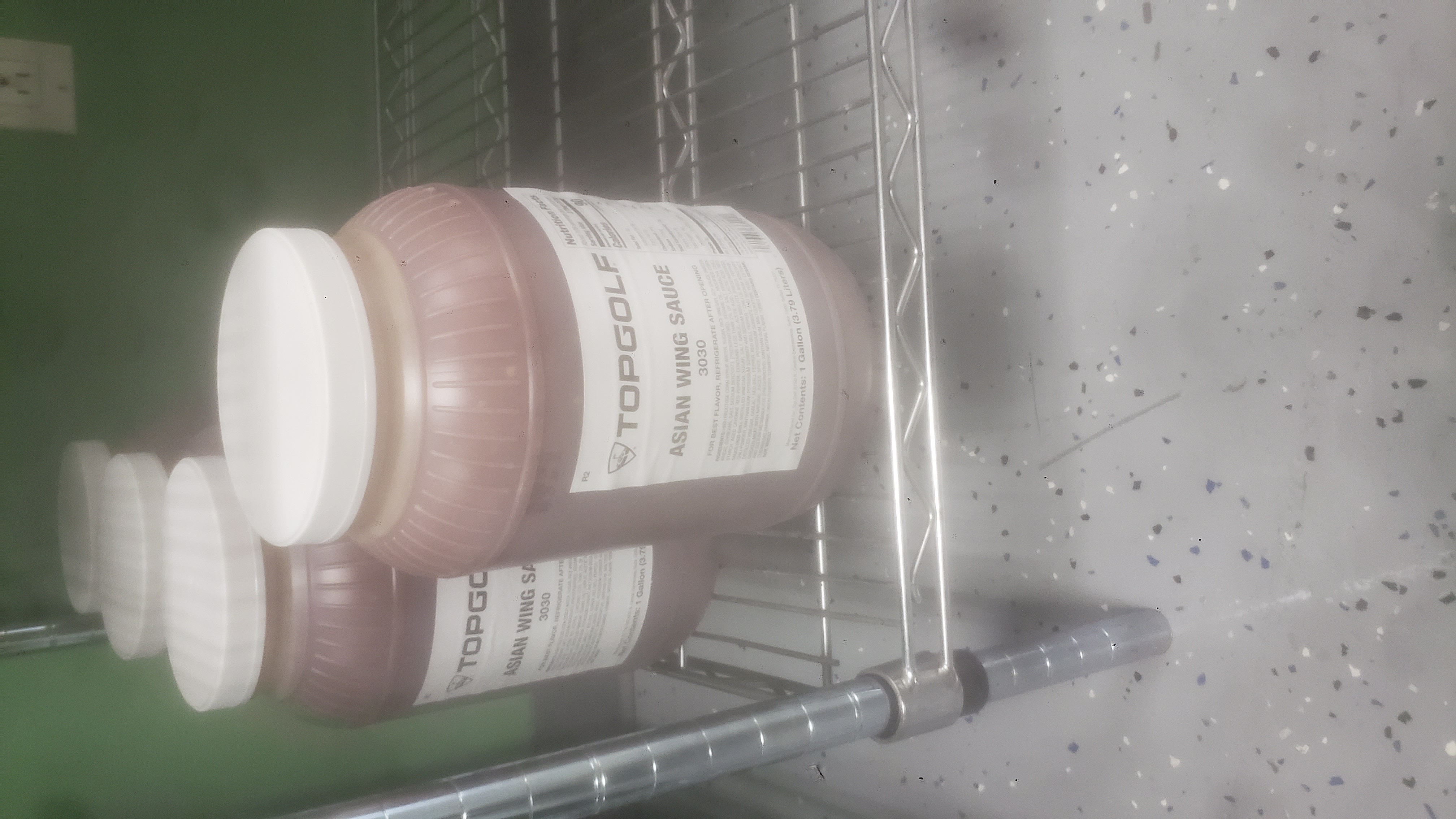 Gallon plastic jars of Asian wing sauce on a shelf.