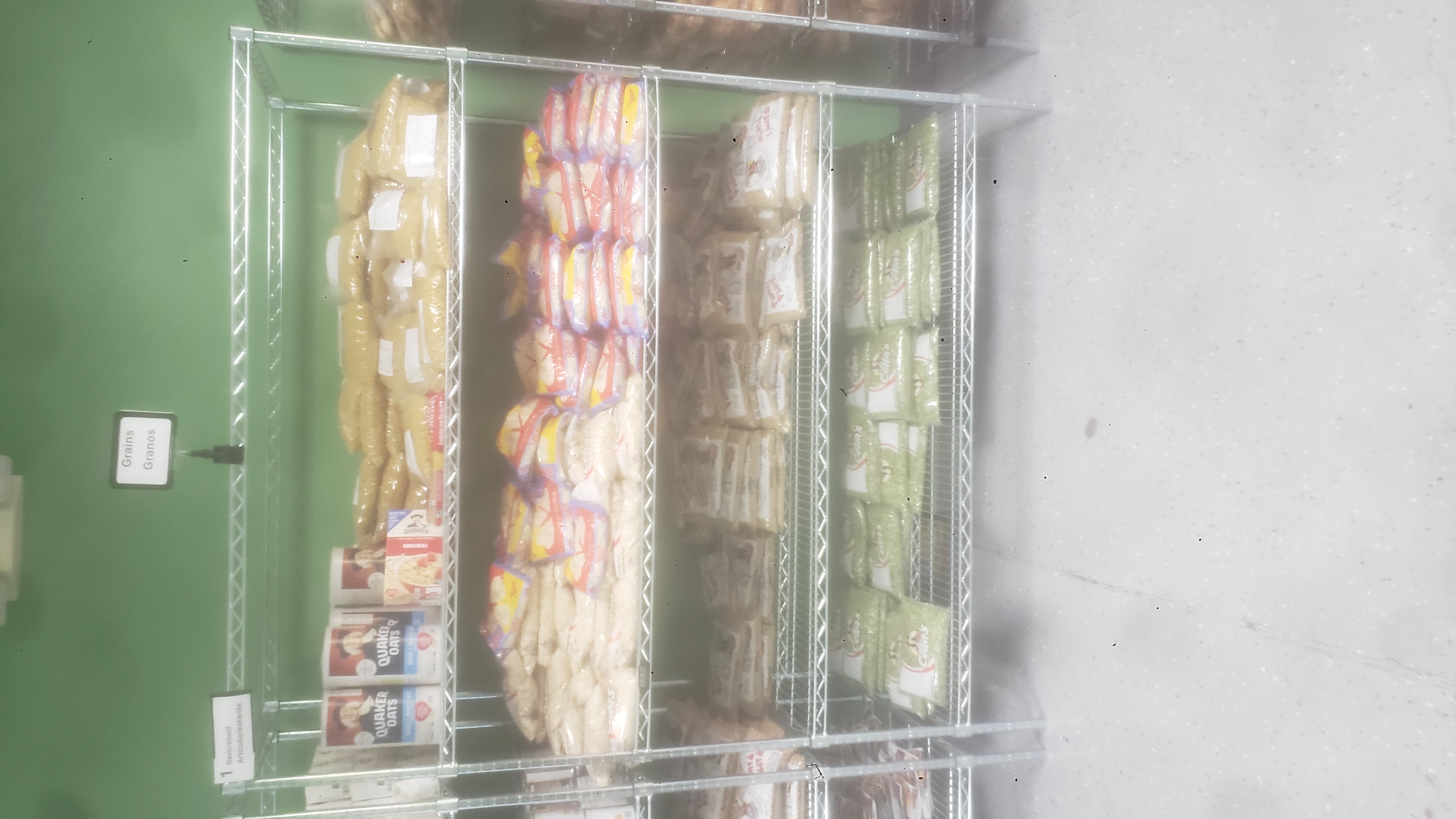 Bags, box and containers of oatmeals, bags of macaroni, bag of spaghetti, bags of lentils, and bags of split green peas on racks of a shelf.