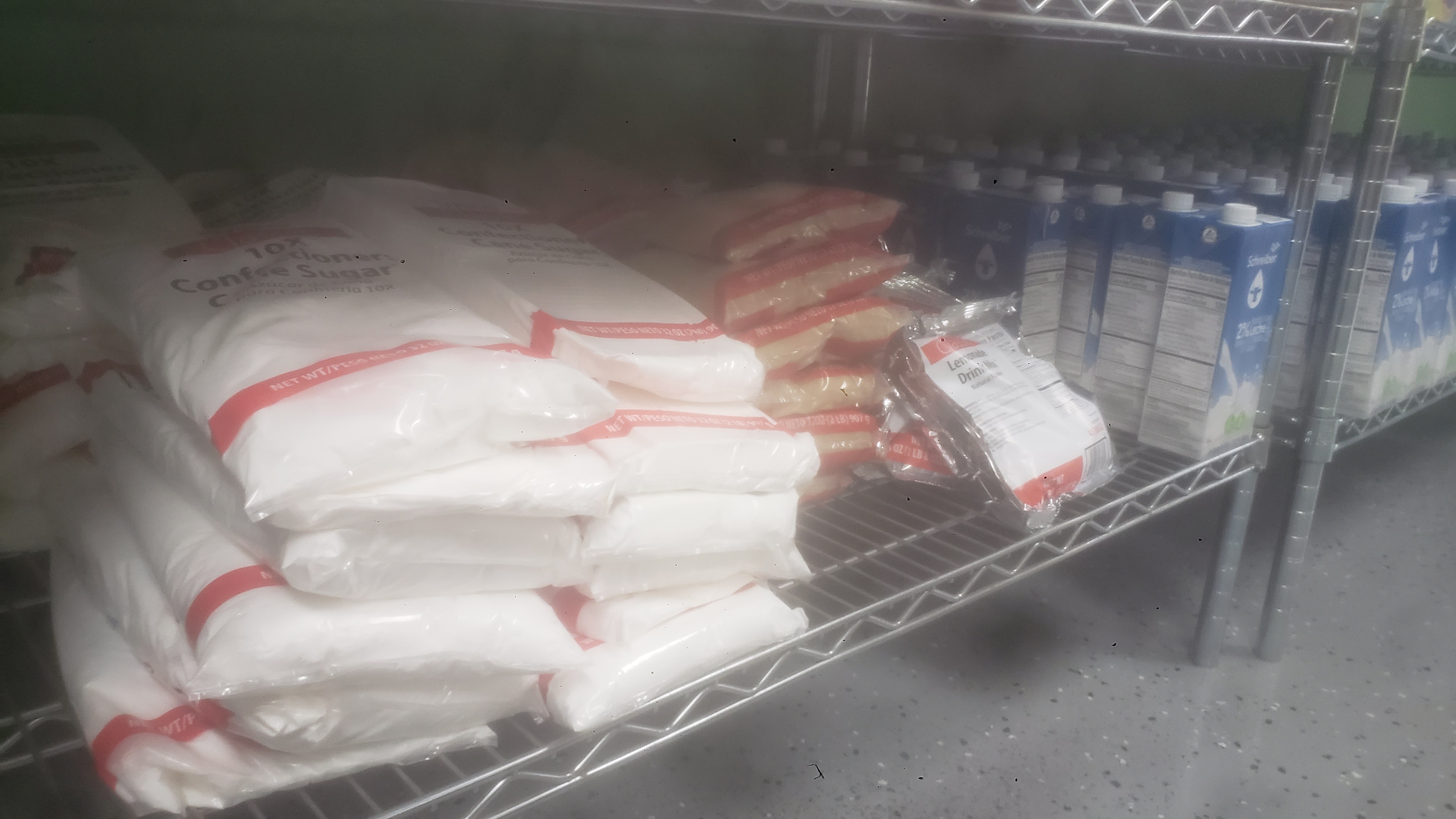 Bags of confectioners sugars, bags of brown sugars, and a bag of lemonade drink mix on a shelf.