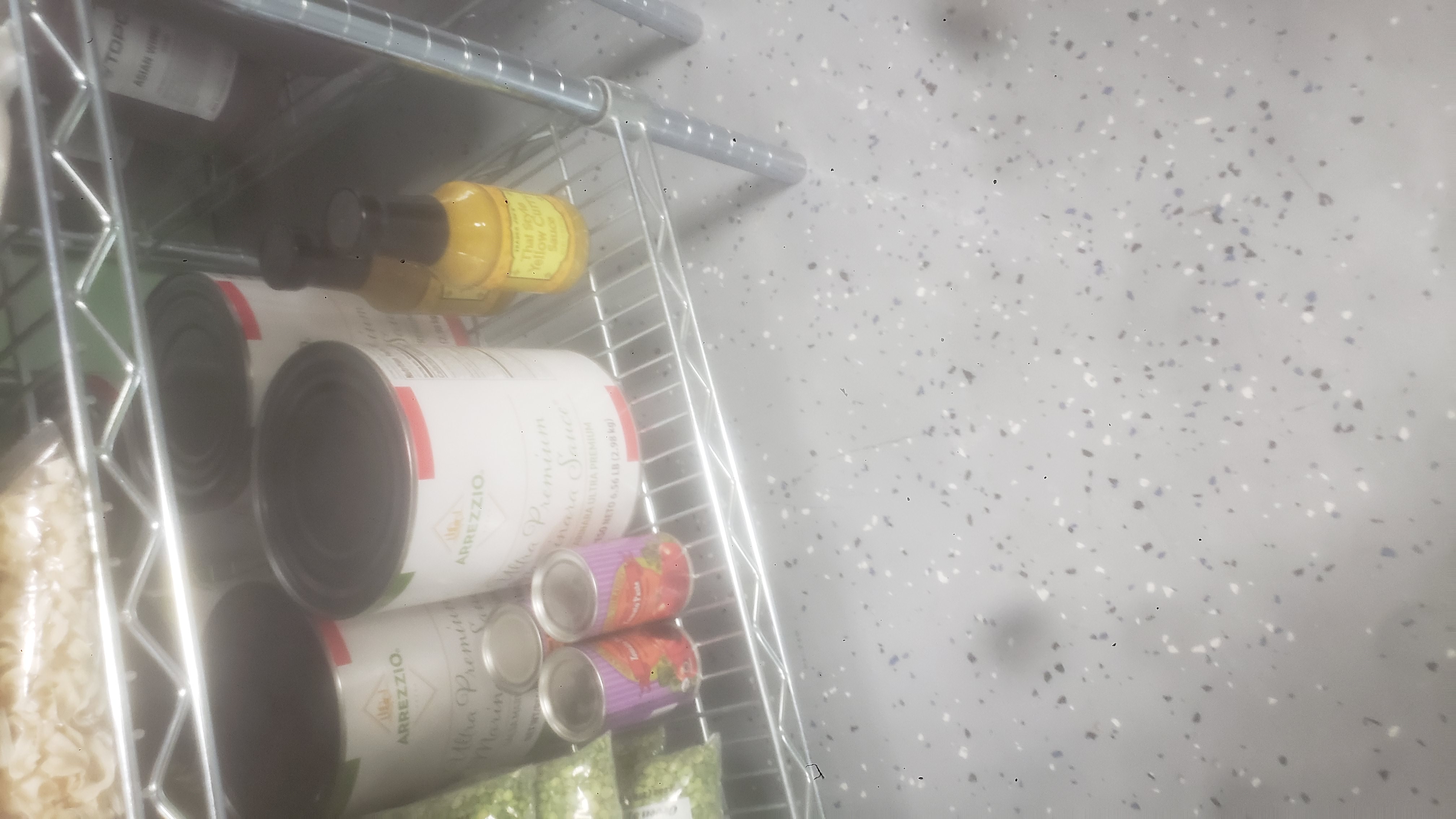 Bags of green split peas, cans of tomato paste, #10 cans of marina sauce, and bottle of Thai style yellow curry sauce on a shelf.