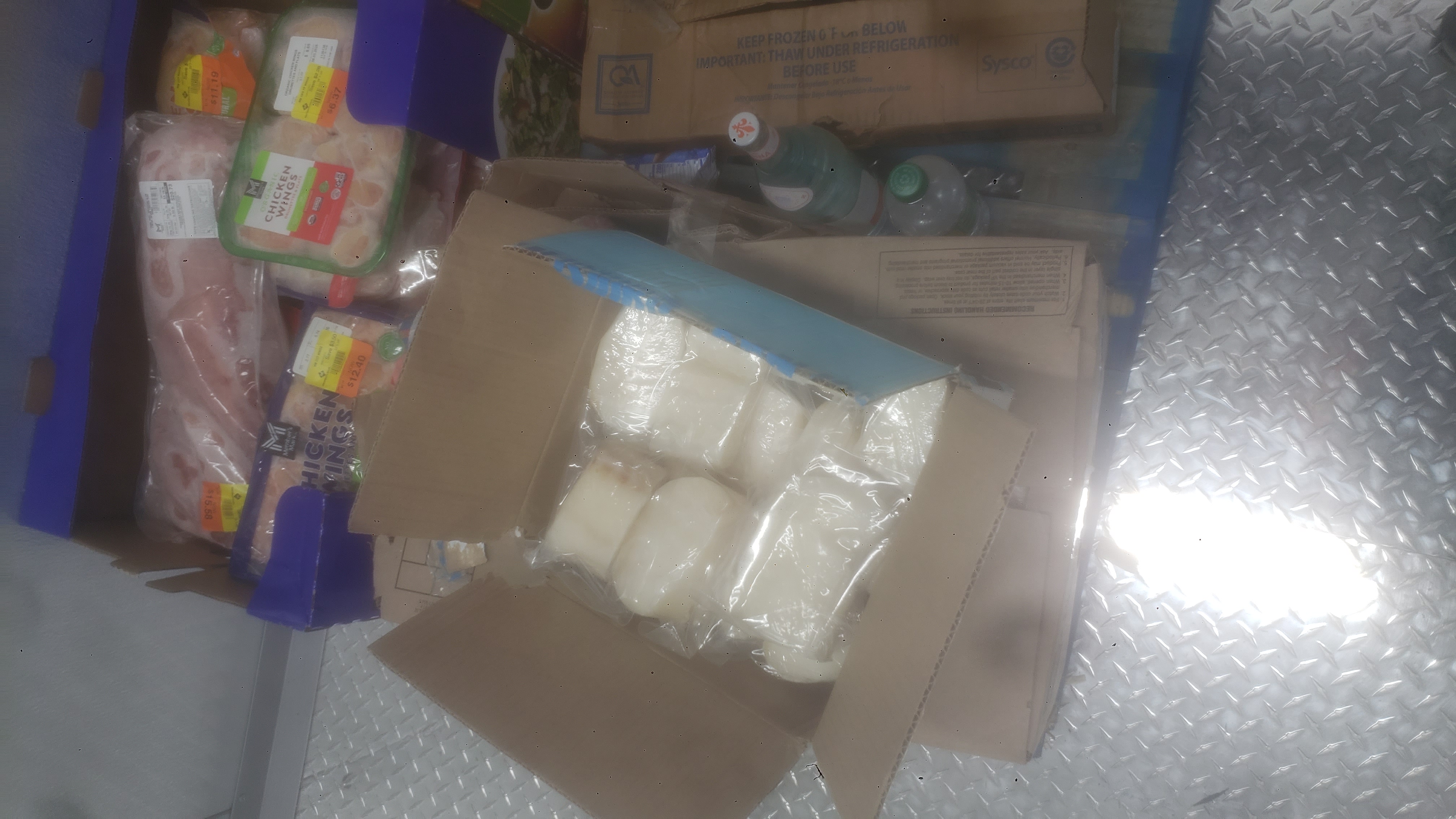 Bottle of water and sprite next to boxes and trays of various meats on a pallet.
