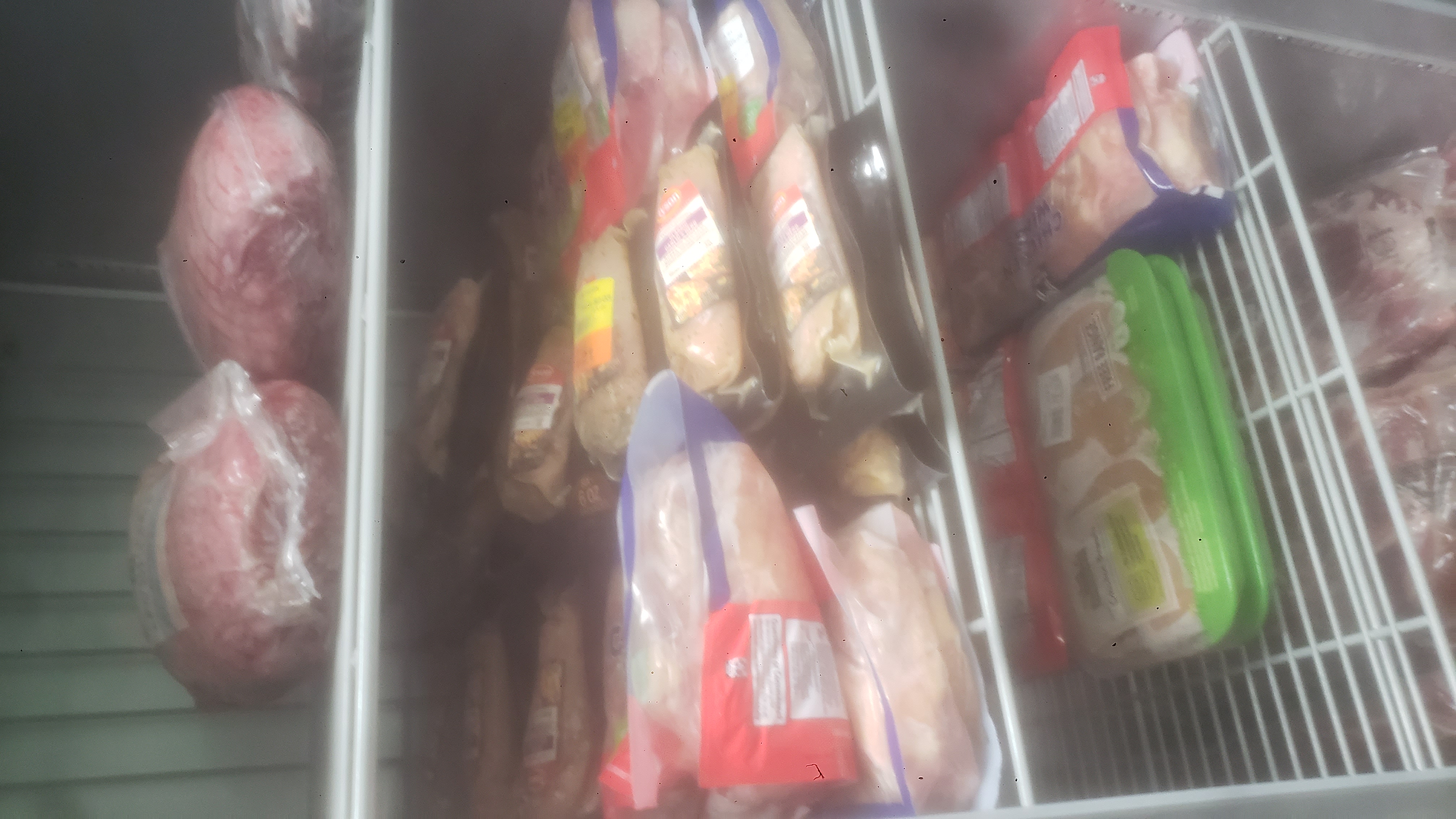 Assorted meats on shelves of a fridge.