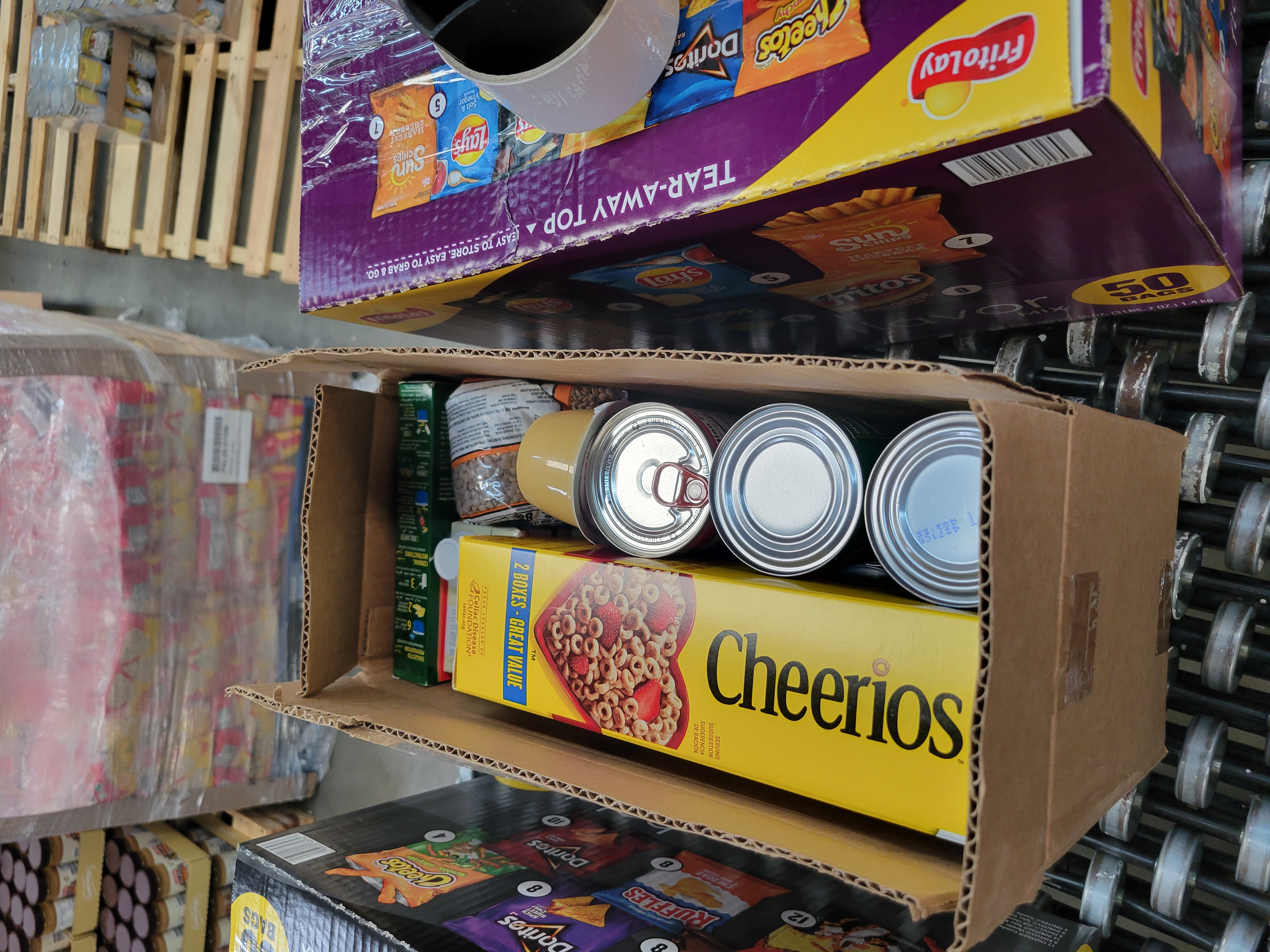 Two chip boxes and one cardboard box full of dry goods with a tape gun on top of one sitting on a conveyor belt.