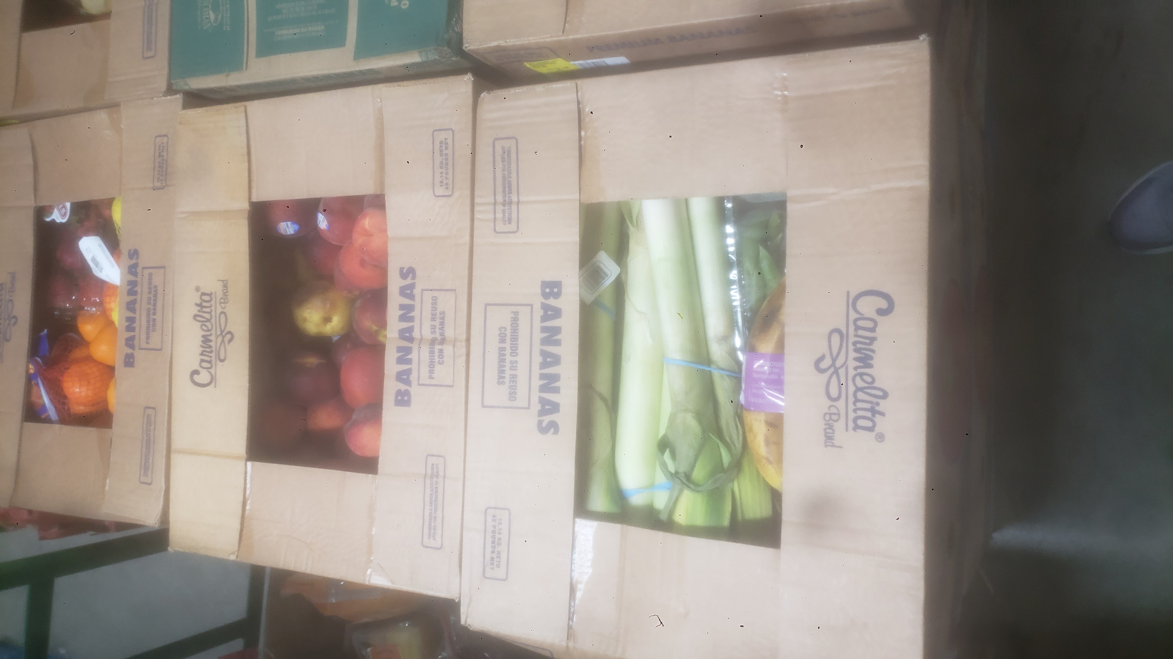 Banana boxes filled with various produce such as peaches, leeks, and oranges.