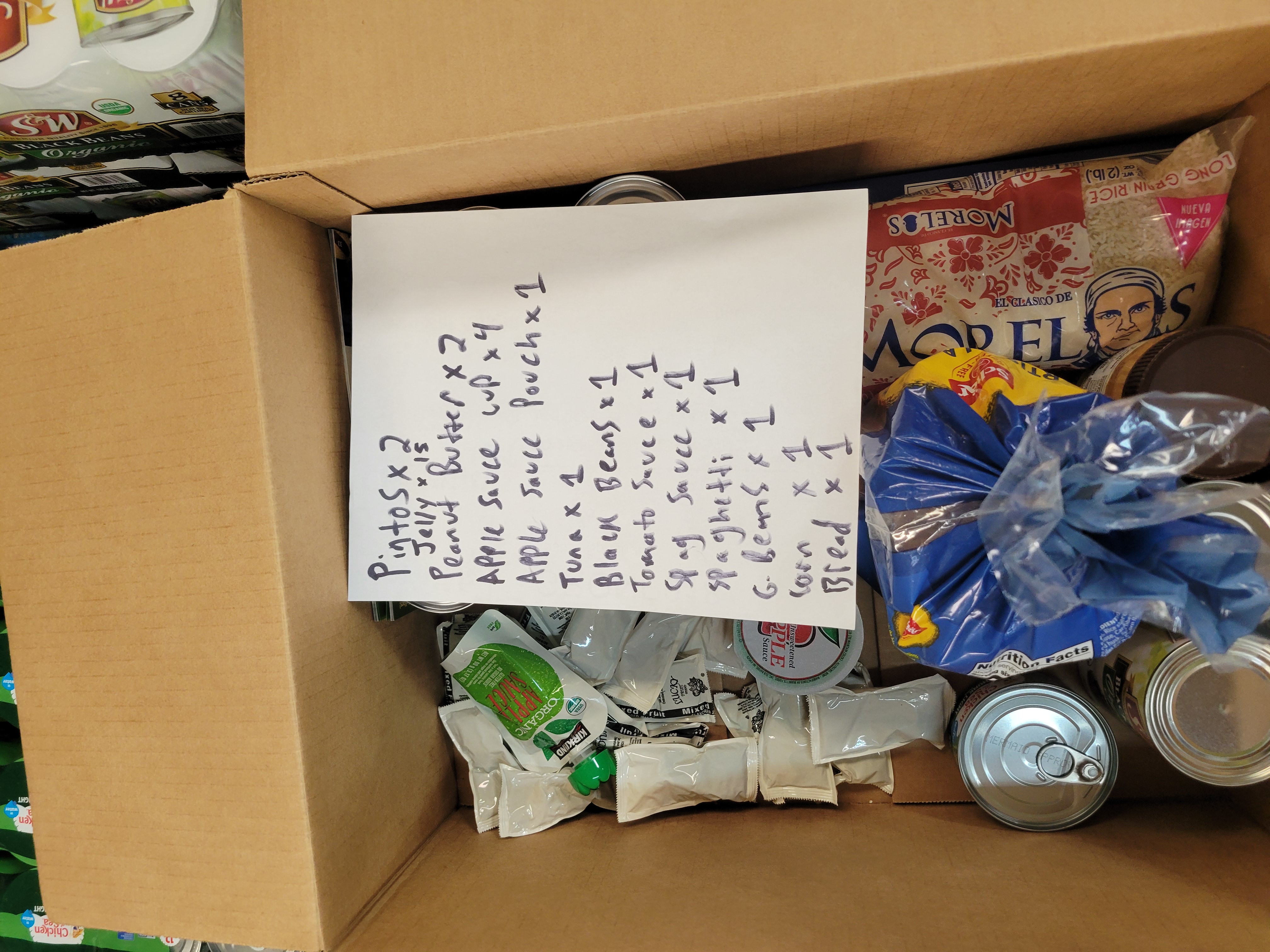 Cardboard box filled with dry goods and a piece of paper with a handwritten list of what needs to be in a box.