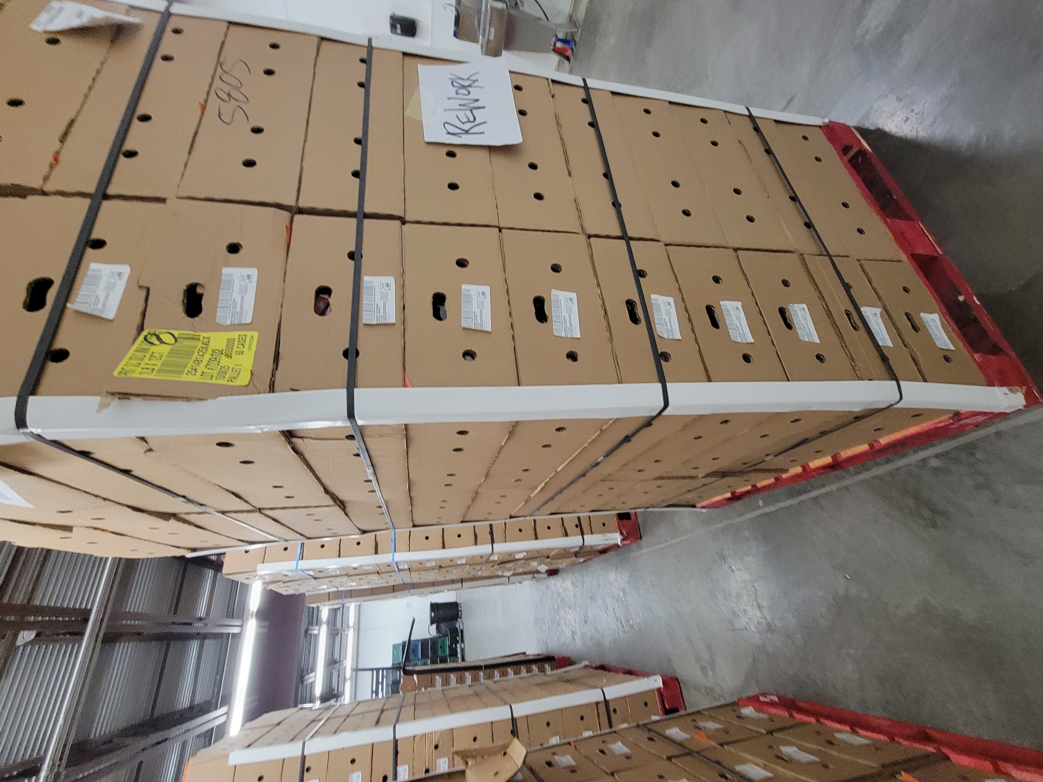 A large shipment of packaged produce stored on pallets with one pallet specifically marked with a sign that says rework.