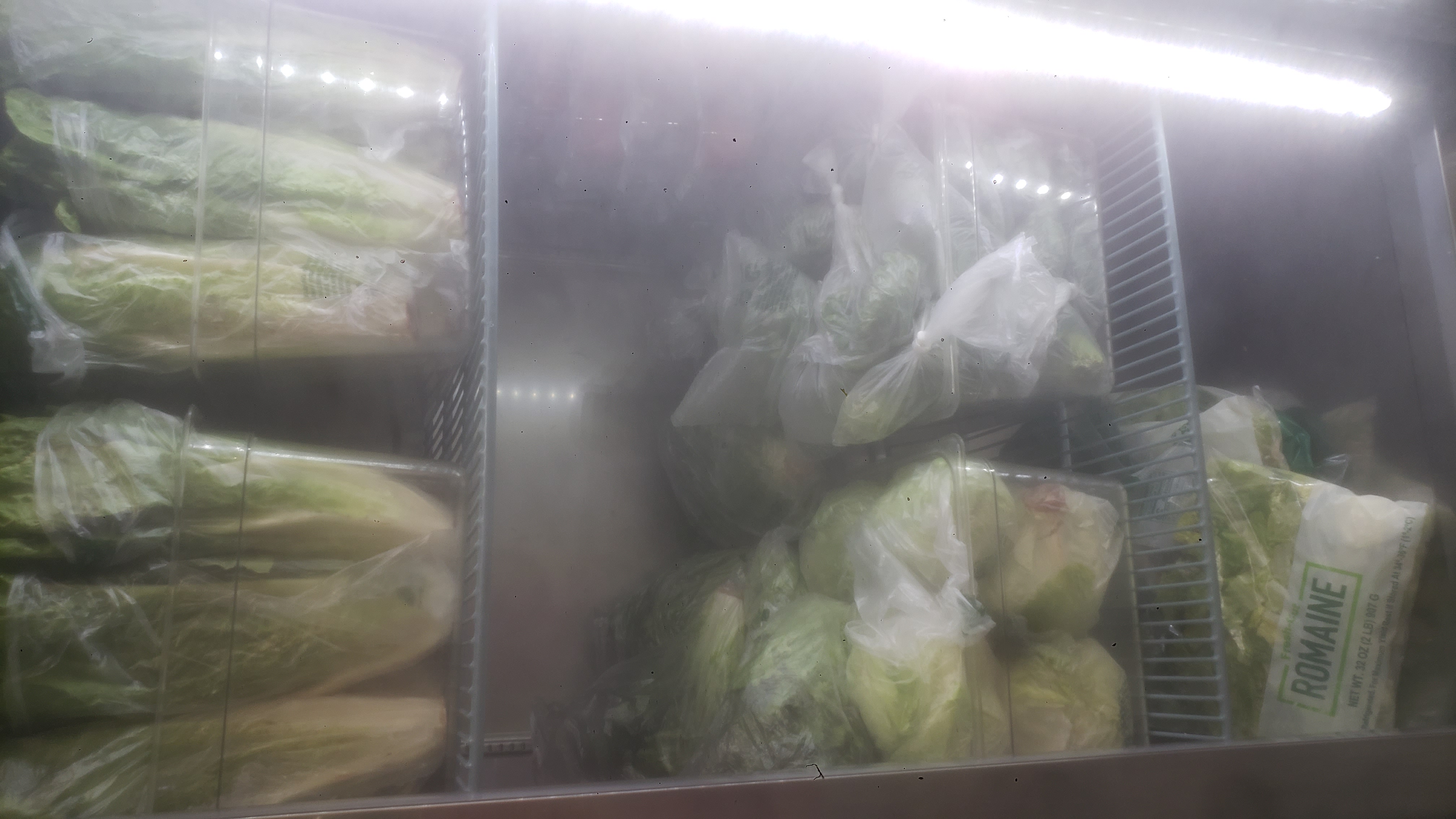 Various greens in containers and bags in a fridge.