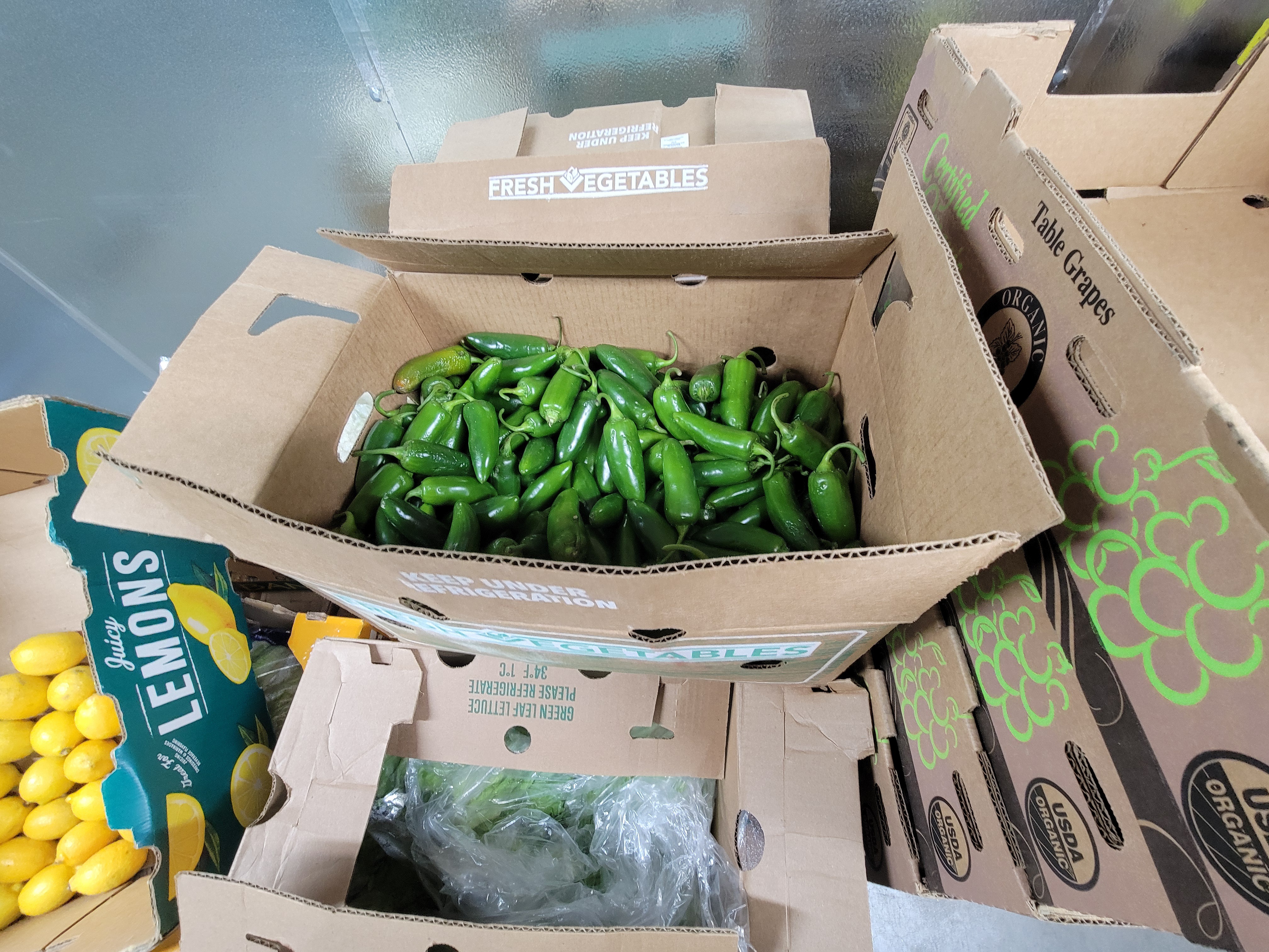 Cardboard box filled with jalapeño peppers next to tray of lemons.