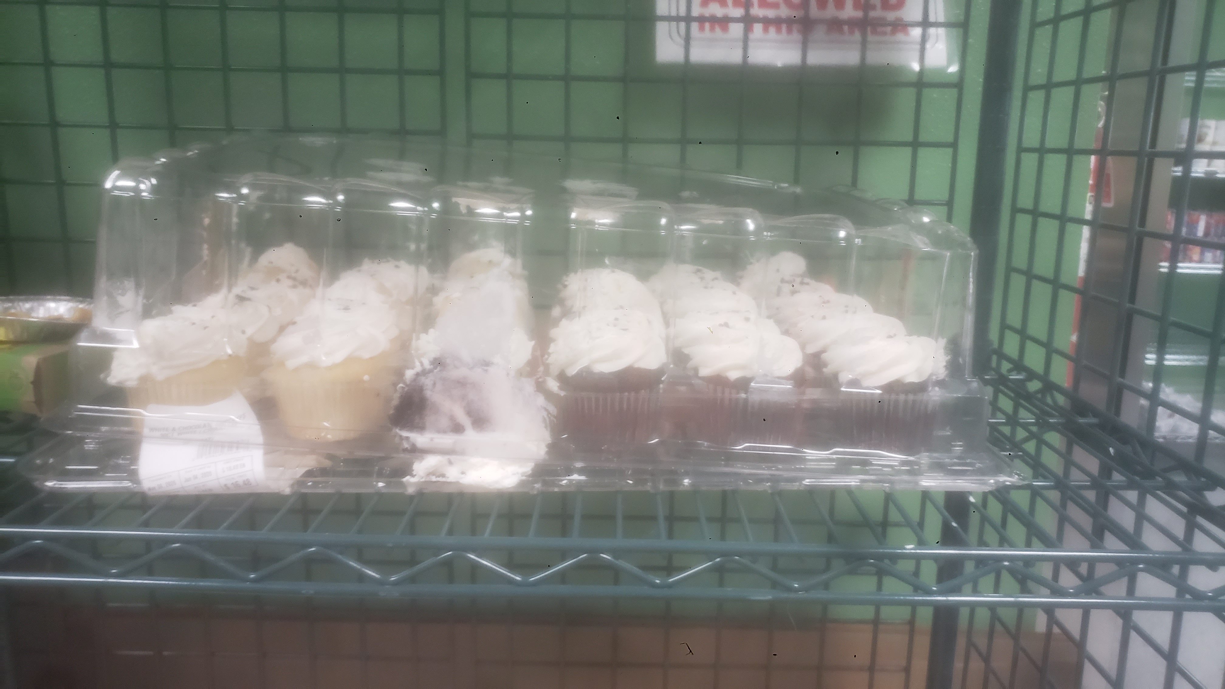 Vanilla and chocolate cupcakes with white frosting and sprinkles in a plasic container.