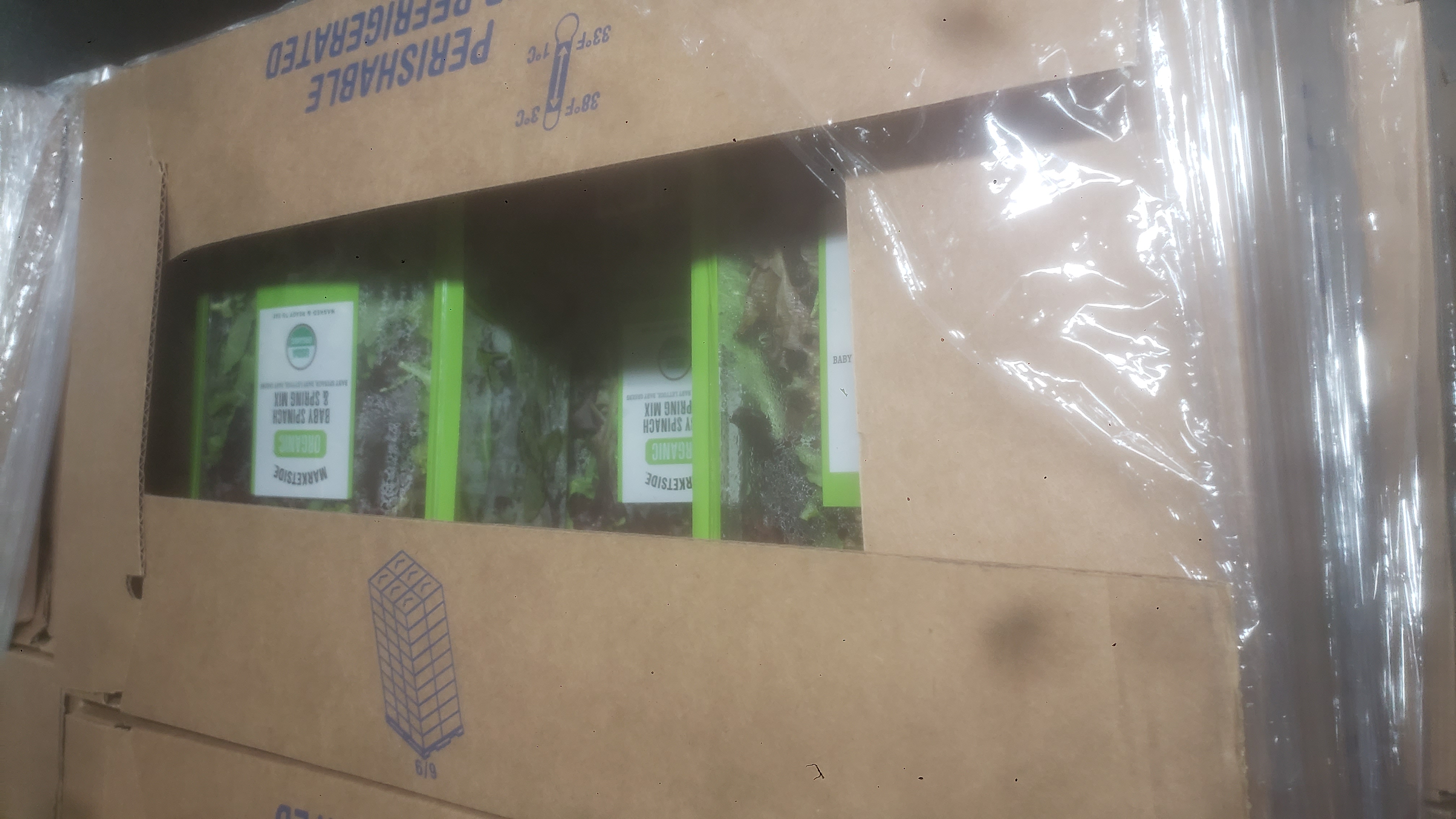 Cardboard boxes filled with containers of baby spinach and spring mix.