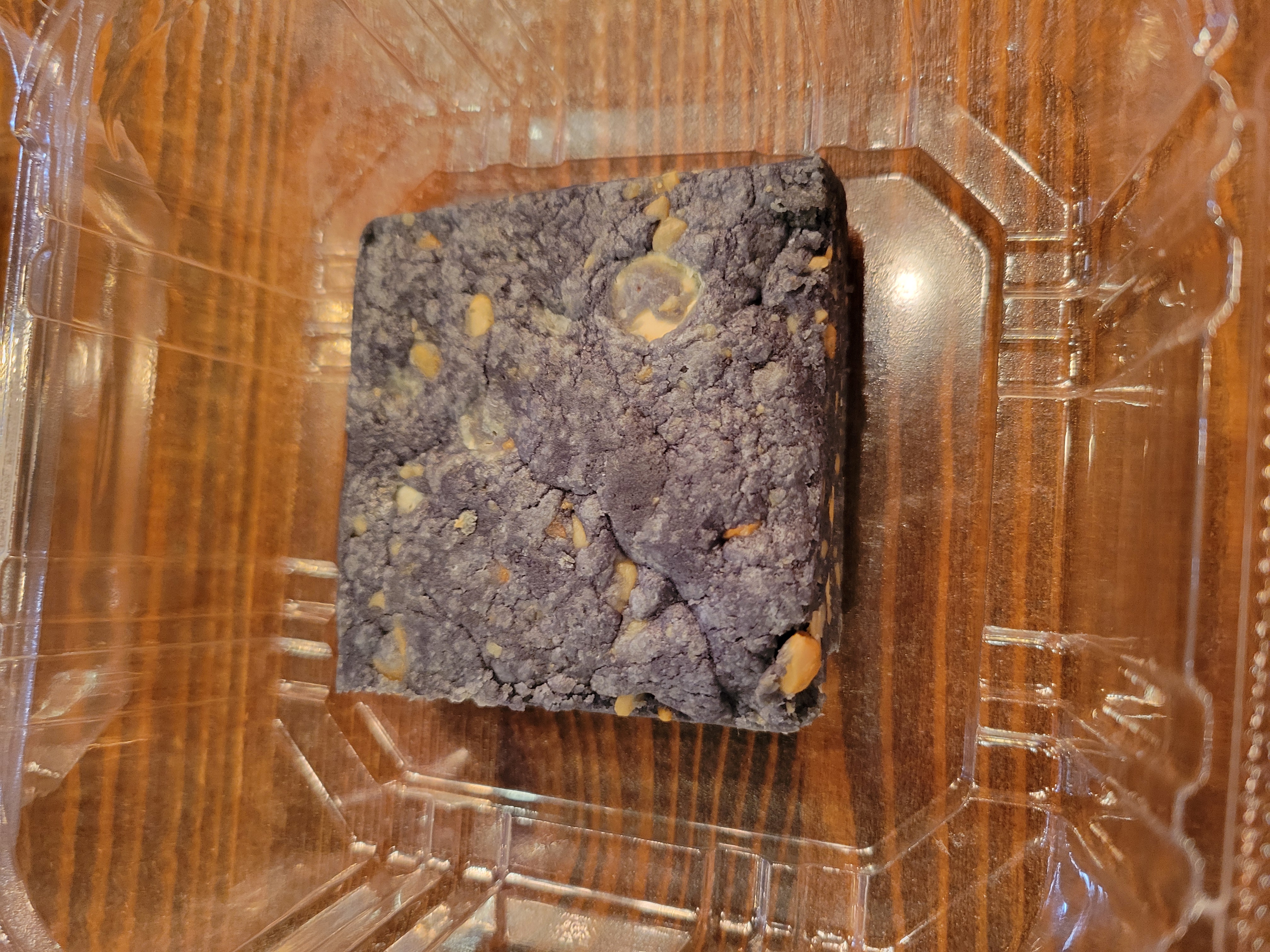 Ube brownie with cashews in a plastic to go container.