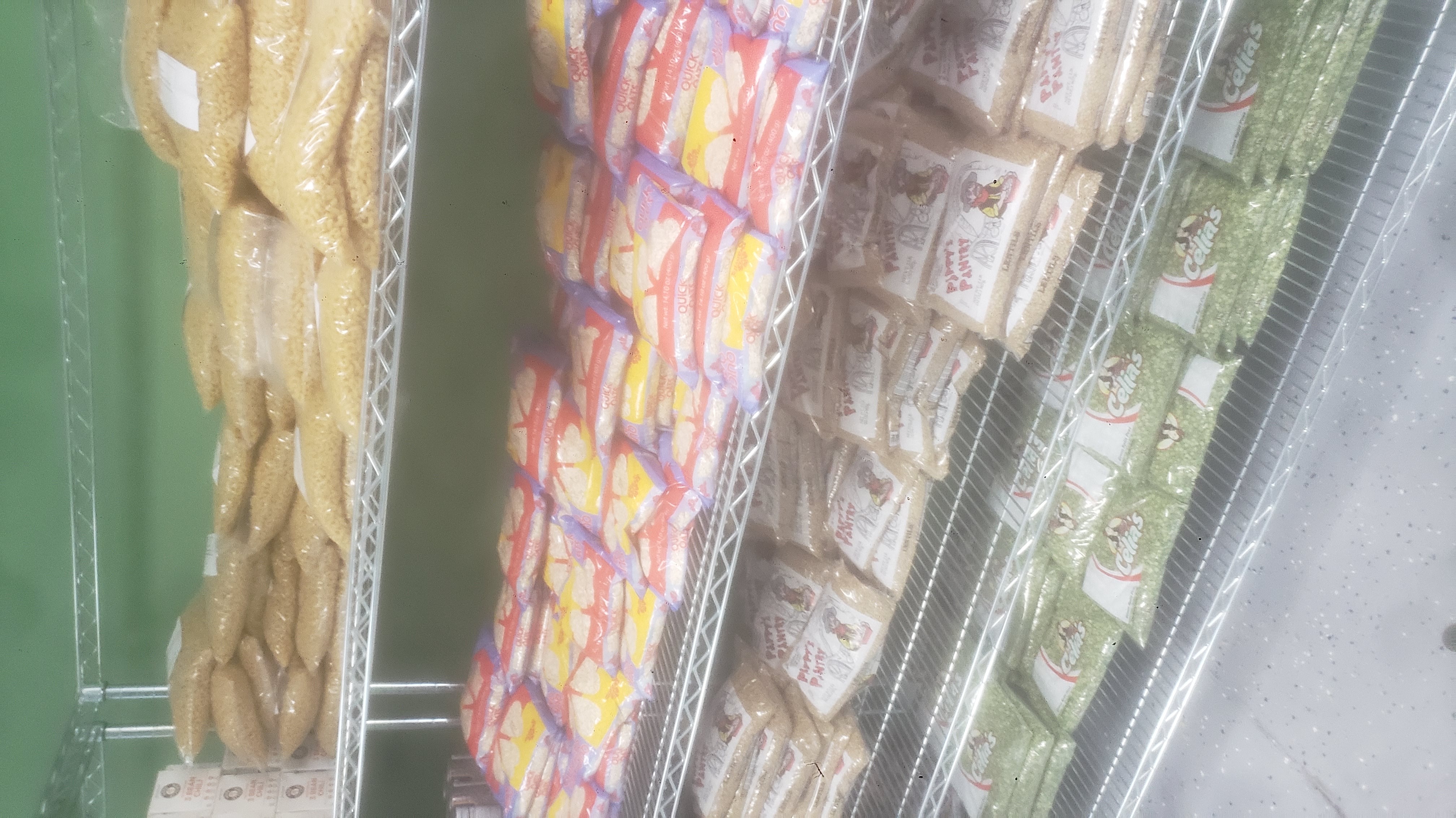 Bags of macaroni, bags of oatmeals, bags of lentils, and bags of split green peas on racks of a shelf.