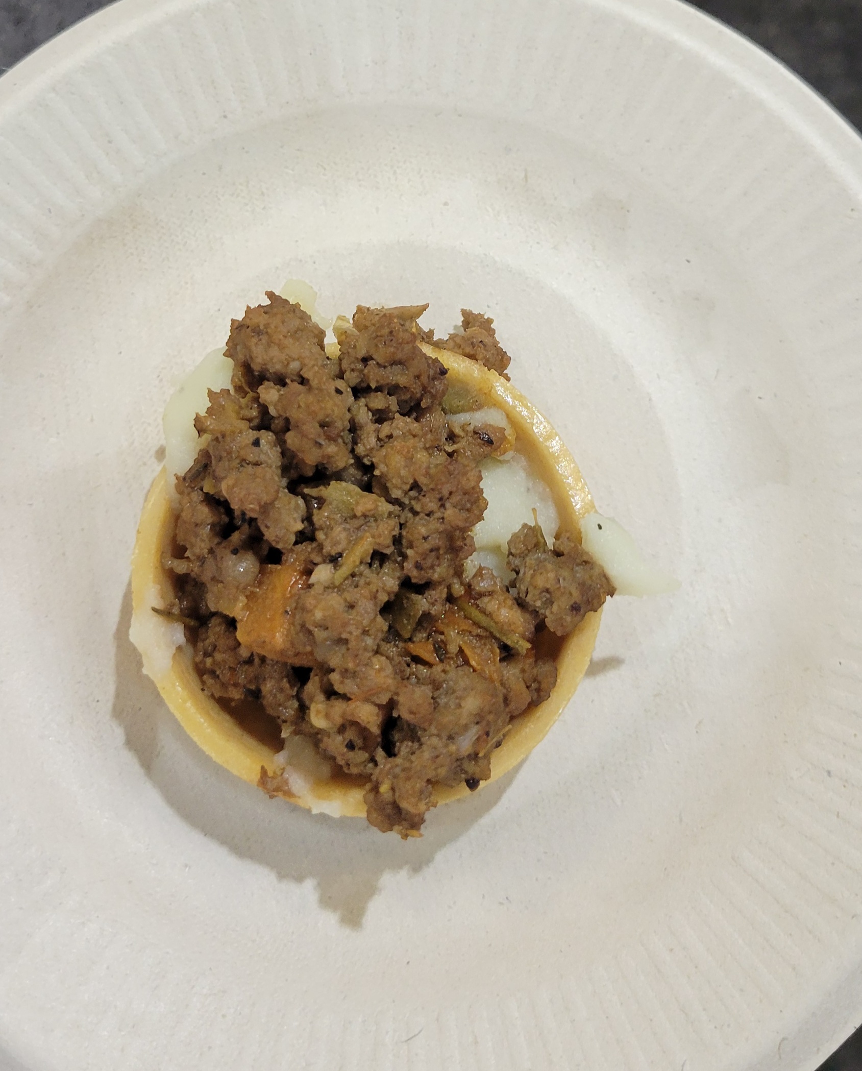 Meat and cheese dish on a mini pie shell on a paper plate.
