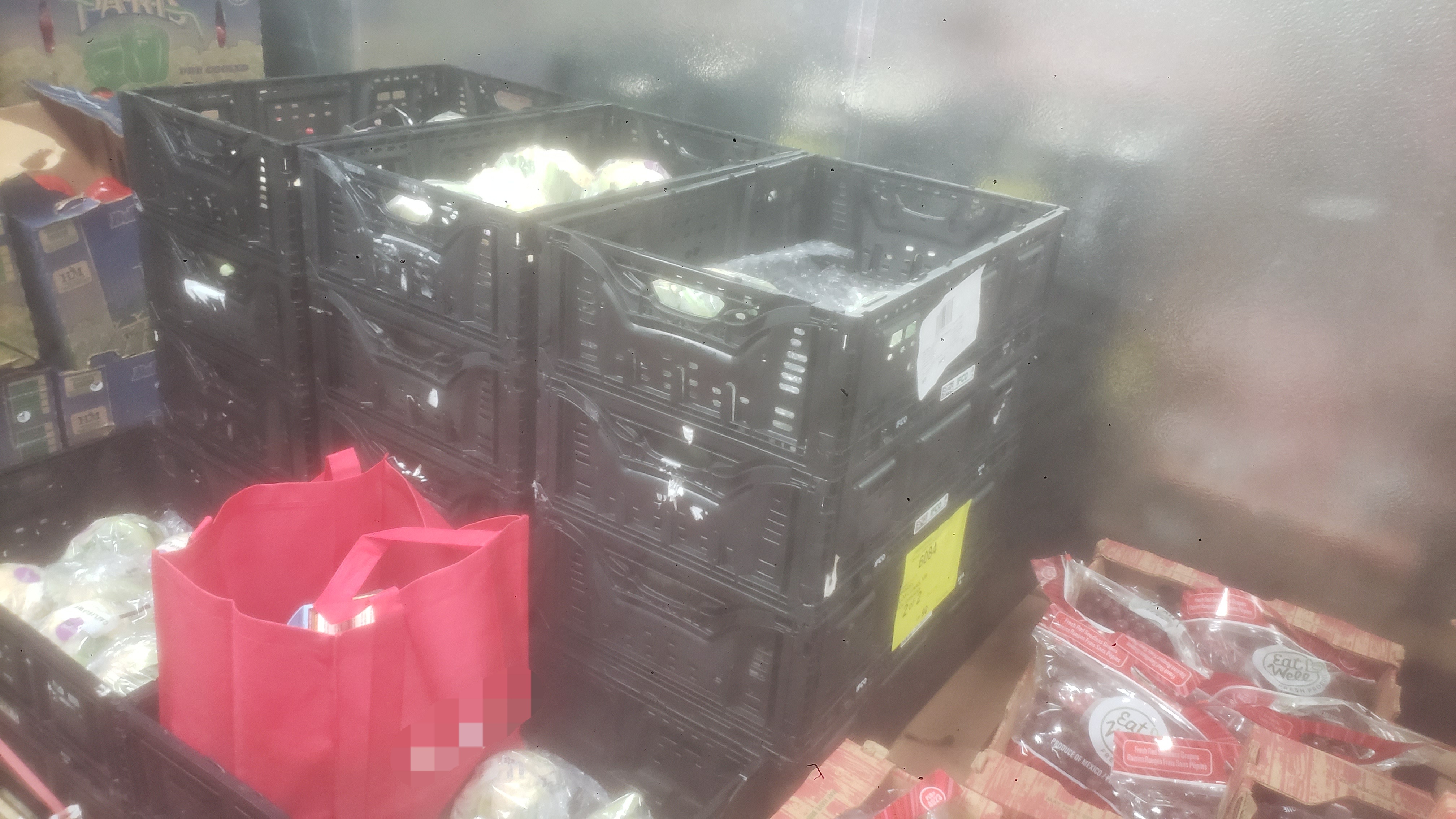 Food filled tote bag on top of crates of lettuce.